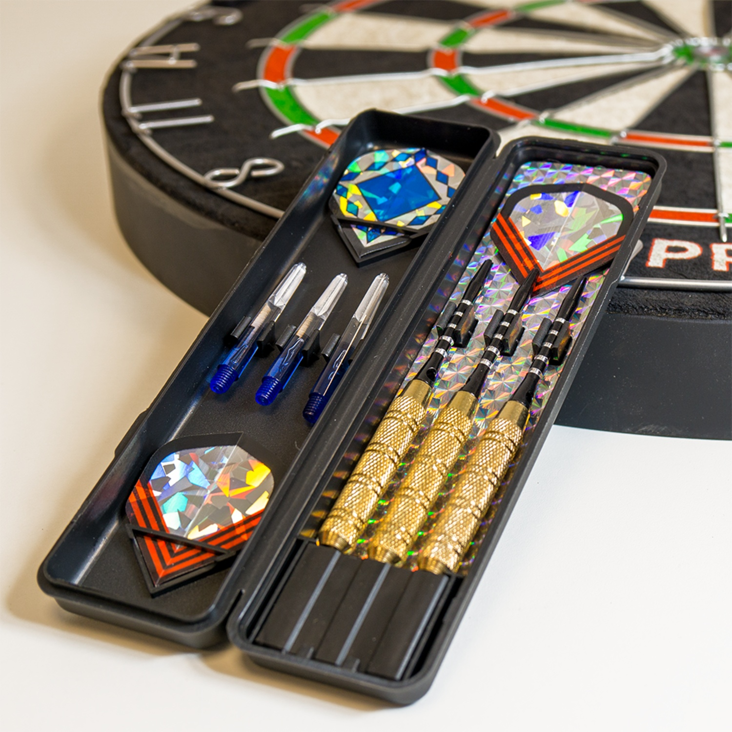 Gold and silver darts with colorful flights in a black case, next to a dartboard.