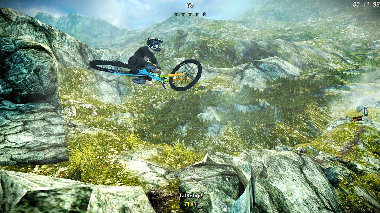 Mountainbiker springt über Felsformationen in bergigem Gelände mit Bäumen.