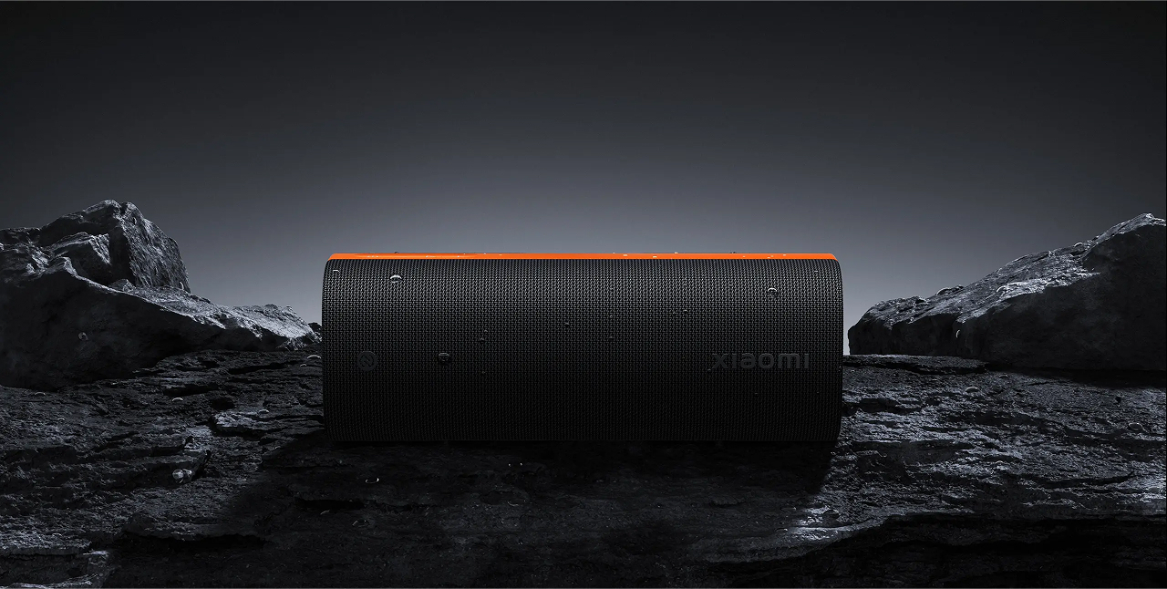 Czarny głośnik Xiaomi z pomarańczowym paskiem na skałach.