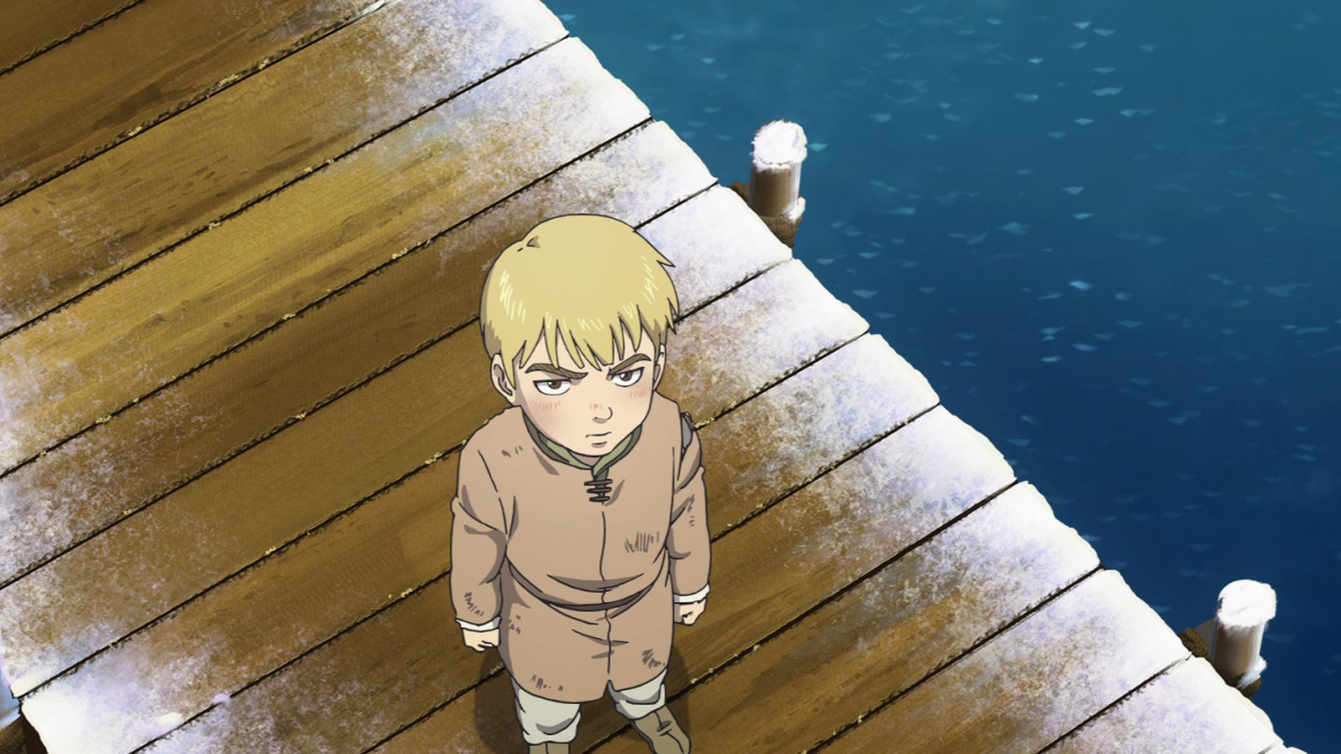 Ein Junge mit blonden Haaren steht auf einem Holzsteg am Wasser.