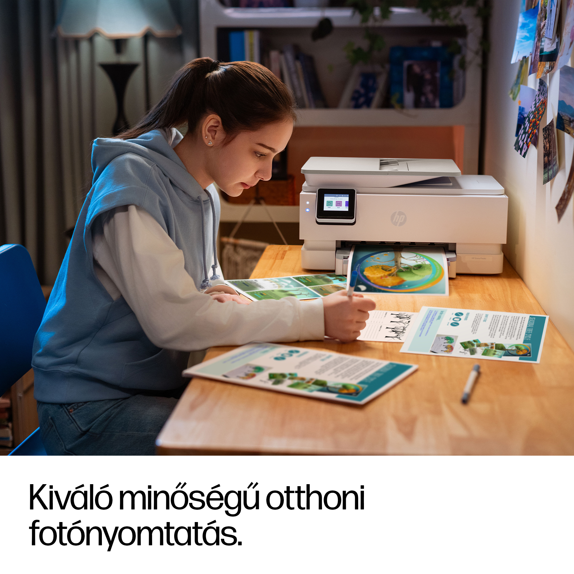 Egy fiatal lány ír az asztalnál, miközben egy nyomtató képet ad ki.