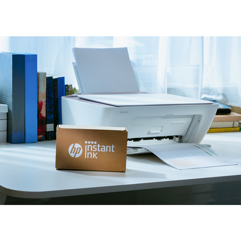 Egy fehér HP nyomtató HP Instant Ink dobozzal az asztalon.