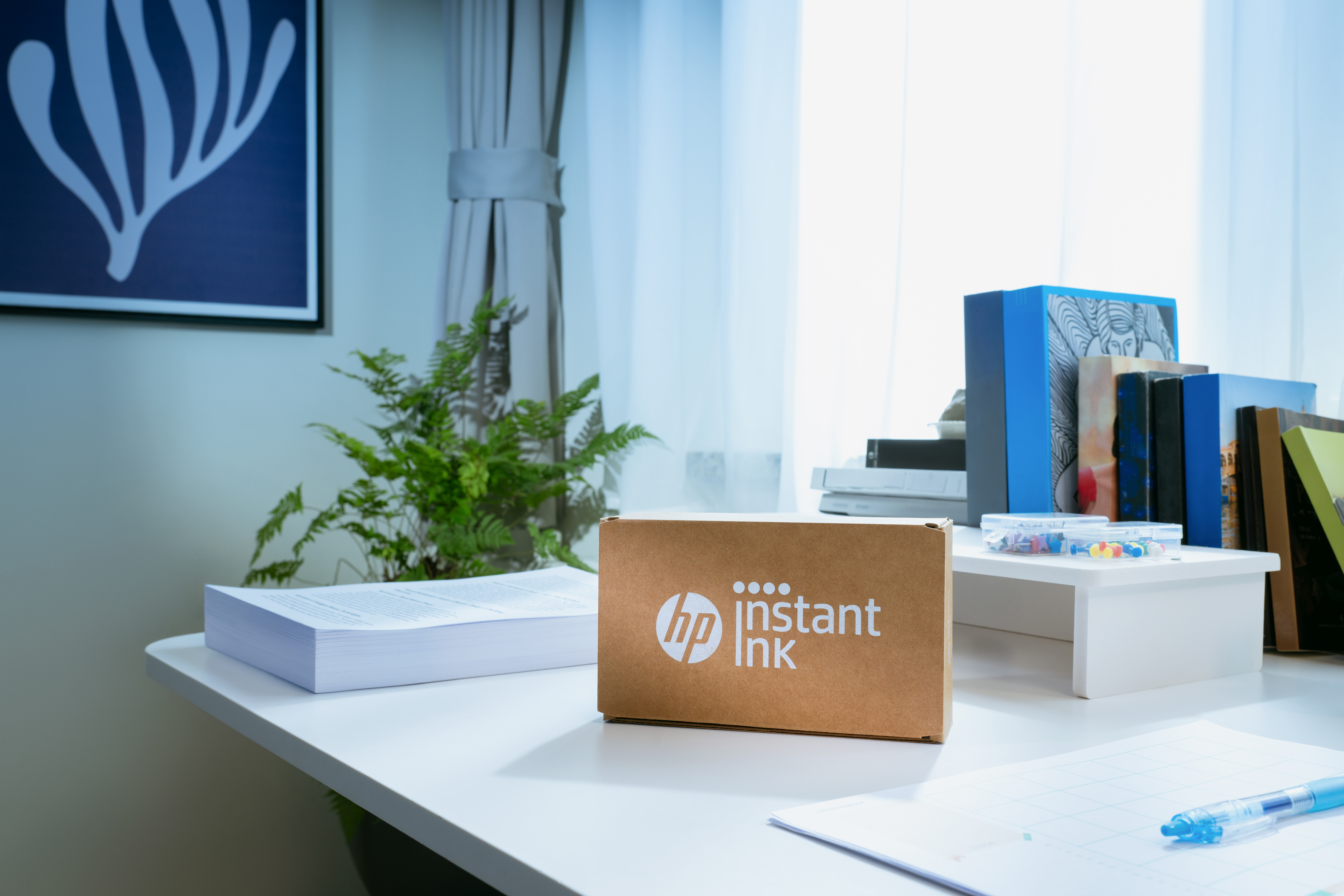 Egy HP Instant Ink doboz papír és könyvek mellett az íróasztalon.
