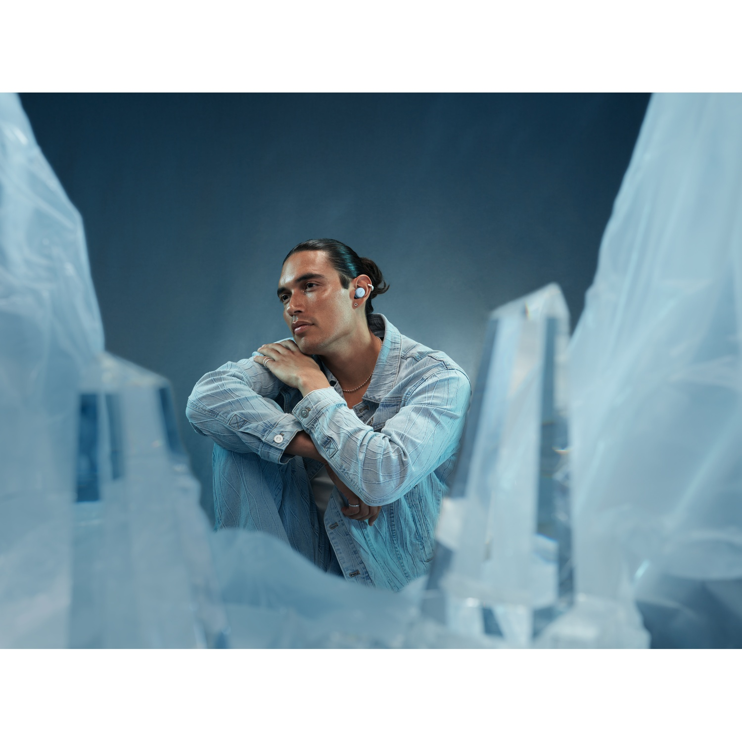 Un homme avec des écouteurs est assis dans un environnement glacial, regardant pensivement à gauche.