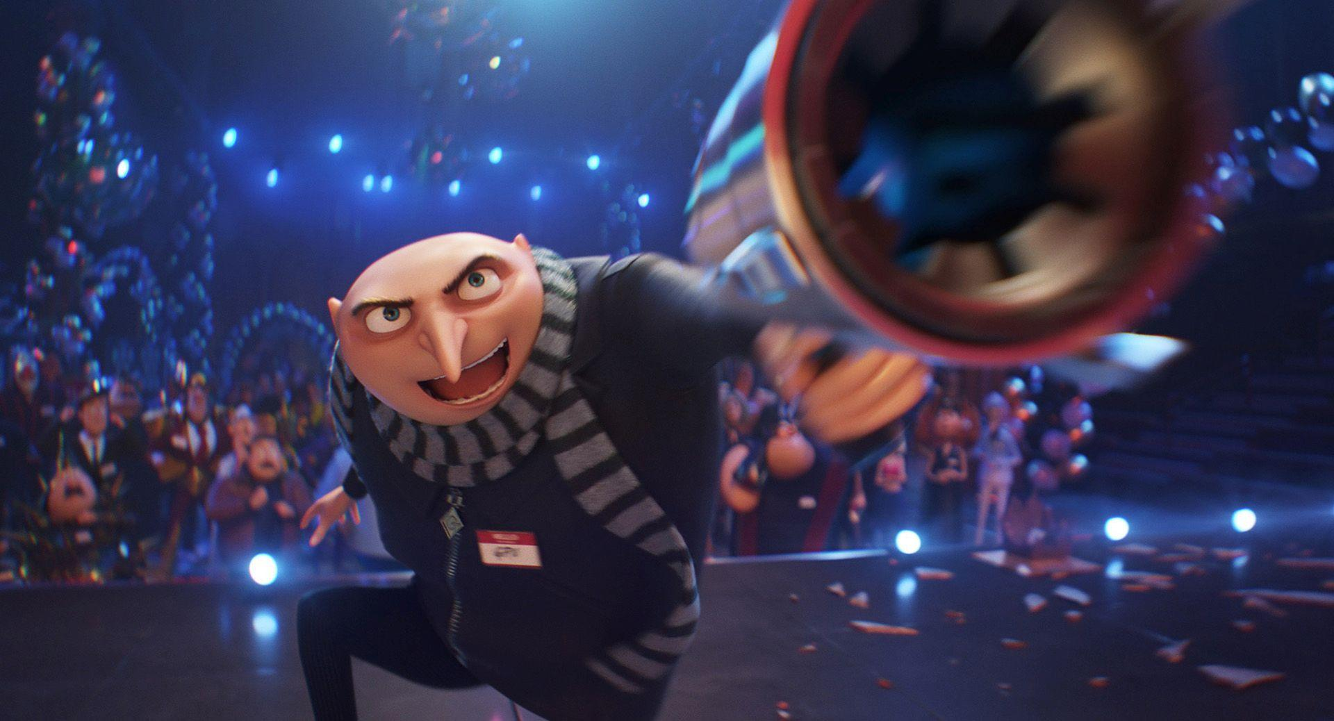 Gru in schwarzem Anzug mit Schal, der eine Waffe hält, vor einem Publikum.