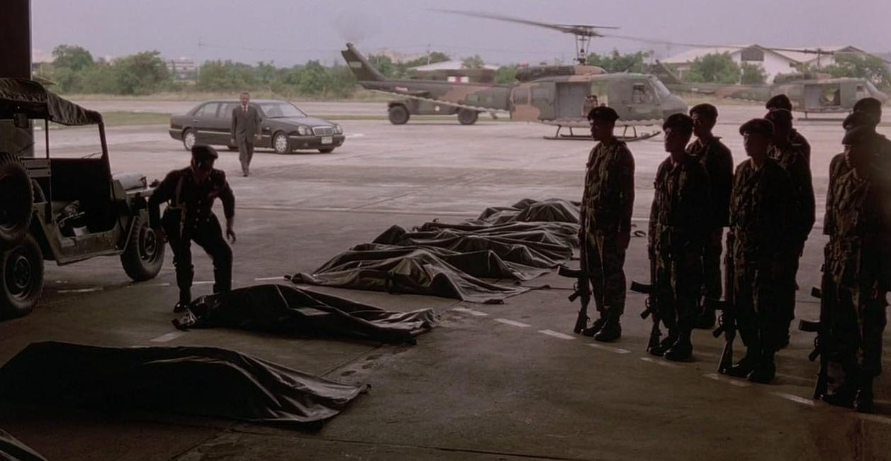 Soldaten stehen Spalier vor Leichensäcken im Hangar; Helikopter und Auto im Hintergrund.
