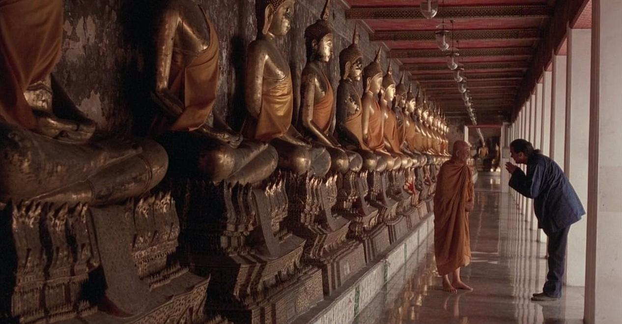 Ein Mönch und ein Mann verbeugen sich vor einer Reihe von goldenen Buddha-Statuen.