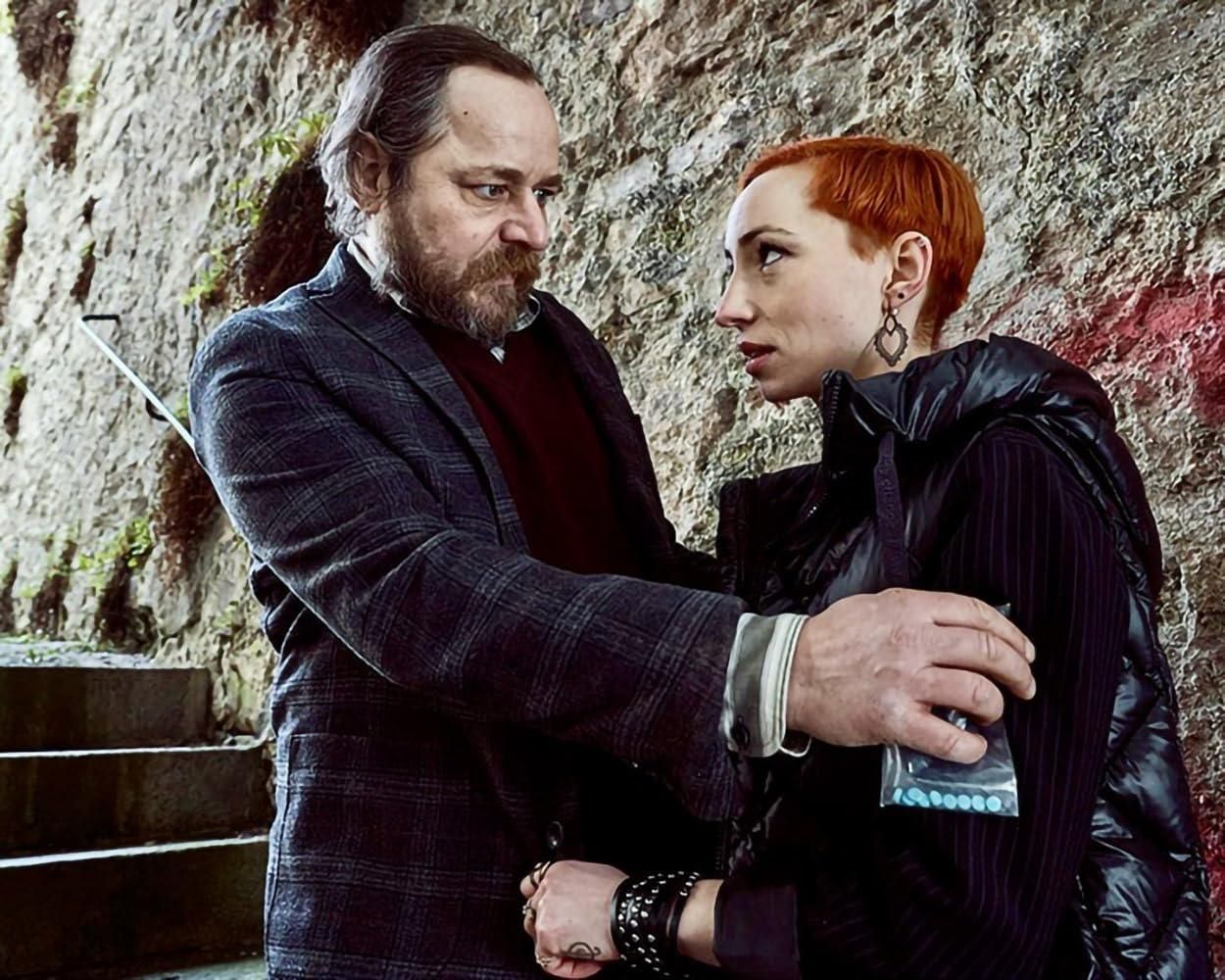 Ein Mann mit Bart und kariertem Jackett legt der Frau mit rotem Haar die Hand auf die Schulter.