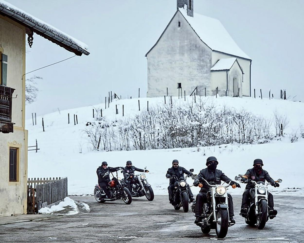 Fünf Motorradfahrer fahren auf einer verschneiten Straße vor einer Kirche.