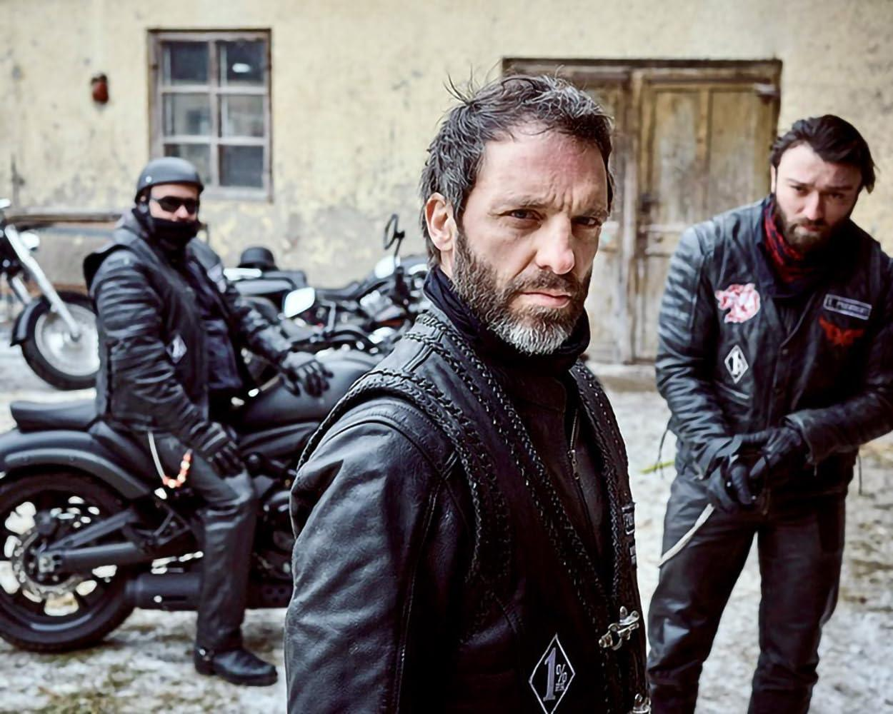 Drei Männer in Lederkleidung stehen vor Motorrädern vor einem Gebäude.