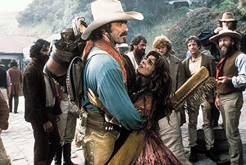 Ein Mann in Cowboykleidung umarmt eine Frau, umgeben von Männern in Kleidung des 19. Jahrhunderts.