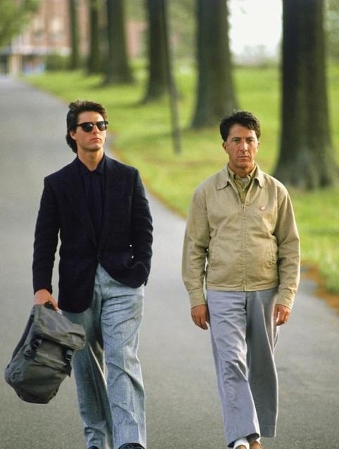 Zwei Männer gehen auf einer Straße zwischen Bäumen. Einer trägt eine Sonnenbrille und eine dunkle Jacke.