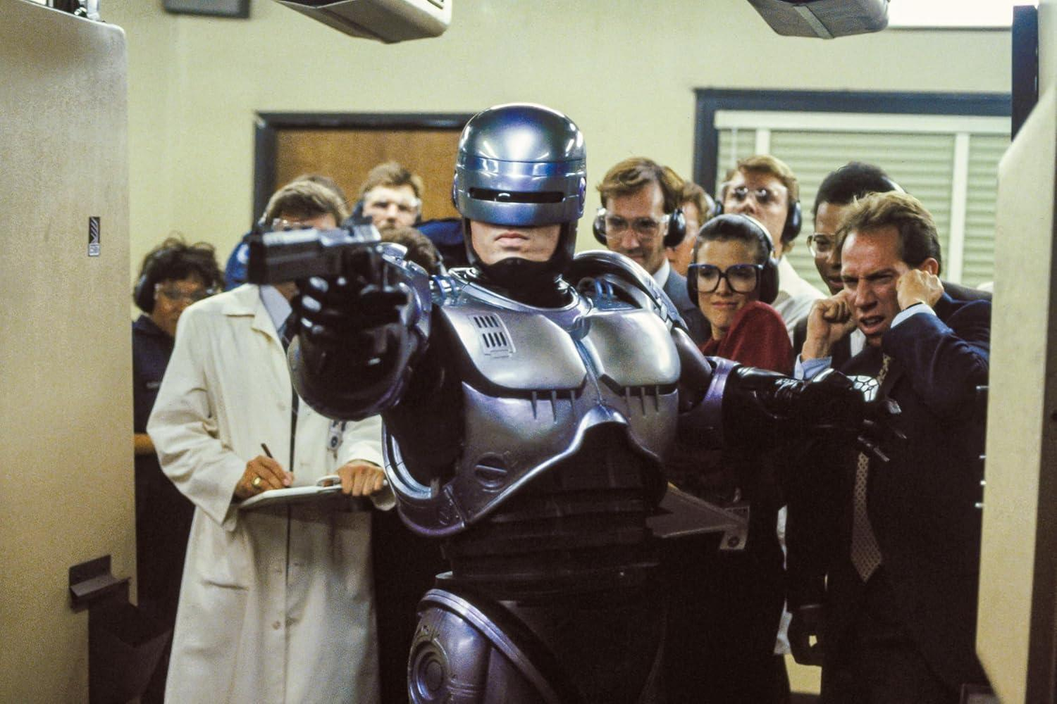 RoboCop zielt mit einer Waffe, umgeben von Menschen, die ihn beobachten.