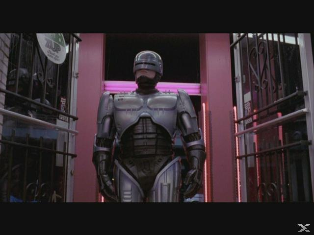 RoboCop steht vor einem neonbeleuchteten Gebäude mit Gittern.