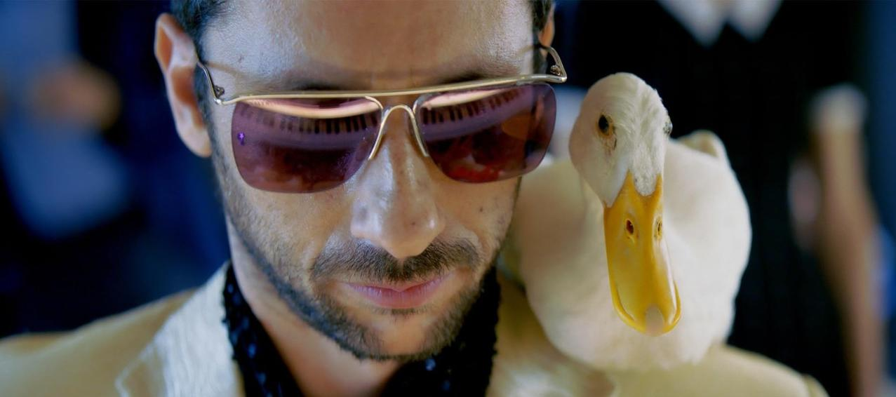 Ein Mann mit Sonnenbrille und eine weiße Ente auf seiner Schulter.