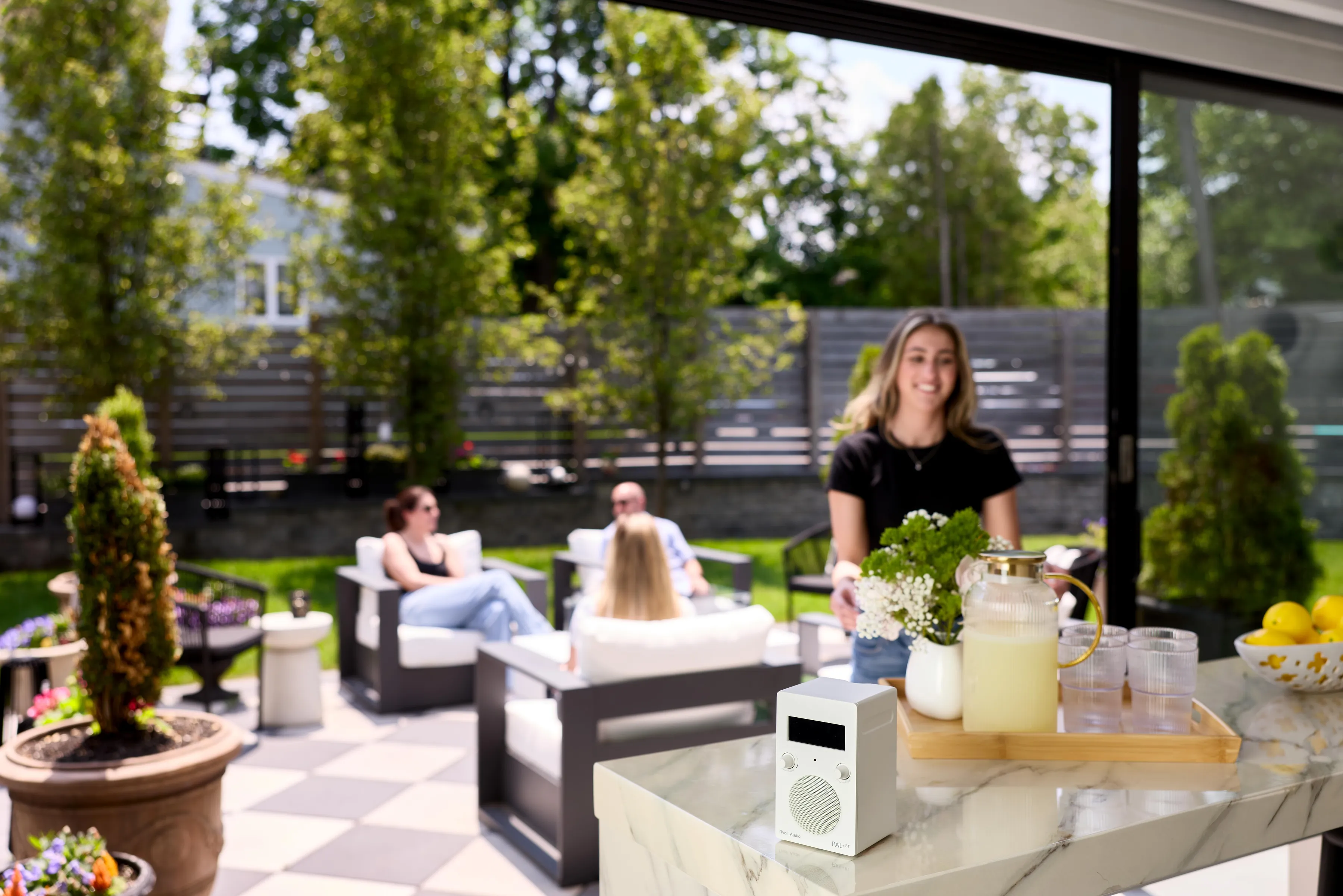 Des gens se détendent sur des chaises blanches dans un jardin. Une table avec des boissons est au premier plan.