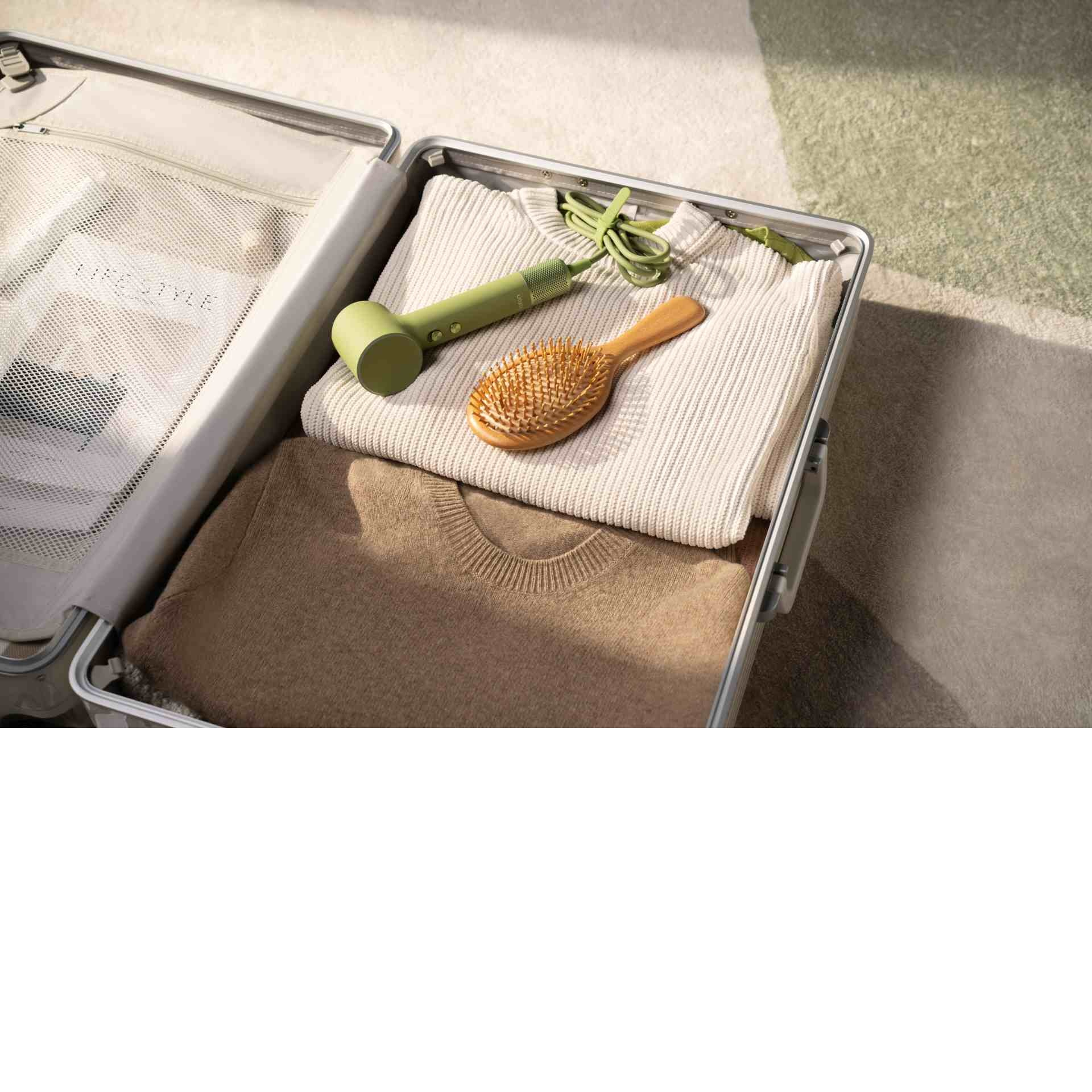 Otwarta walizka z ubraniami, suszarką i szczotką.