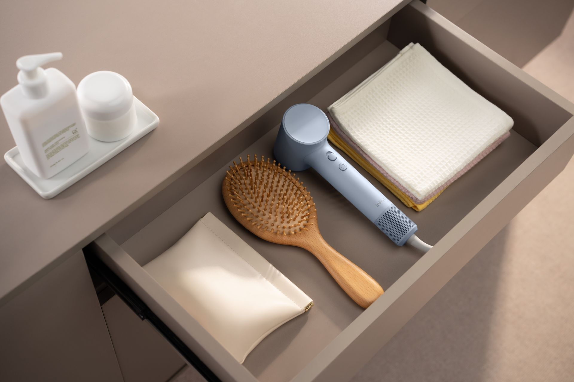 Otwarta szuflada z suszarką, szczotką, kosmetyczką i ręcznikami.