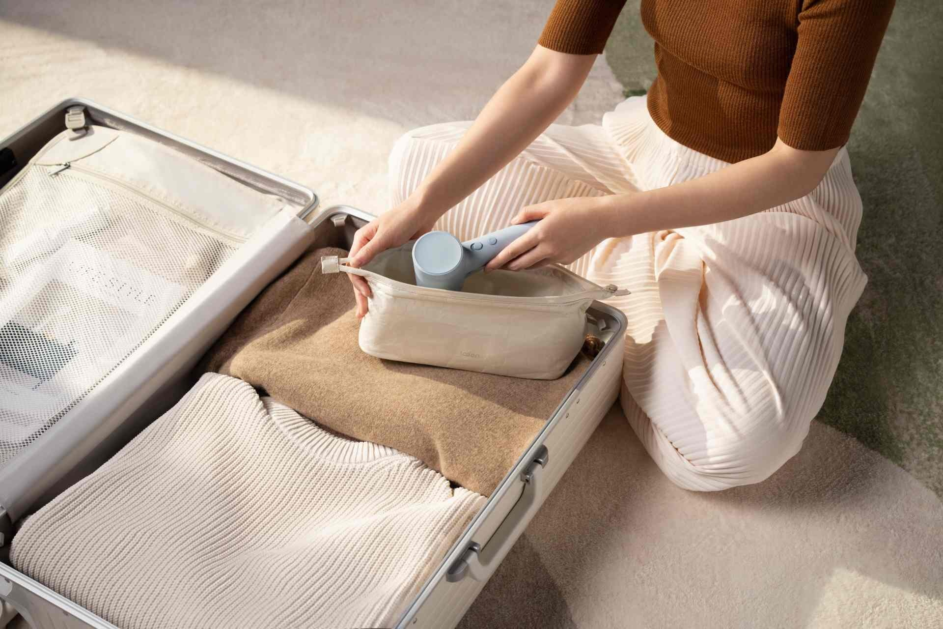 Osoba pakuje walizkę z ubraniami i przenośnym steamerem.