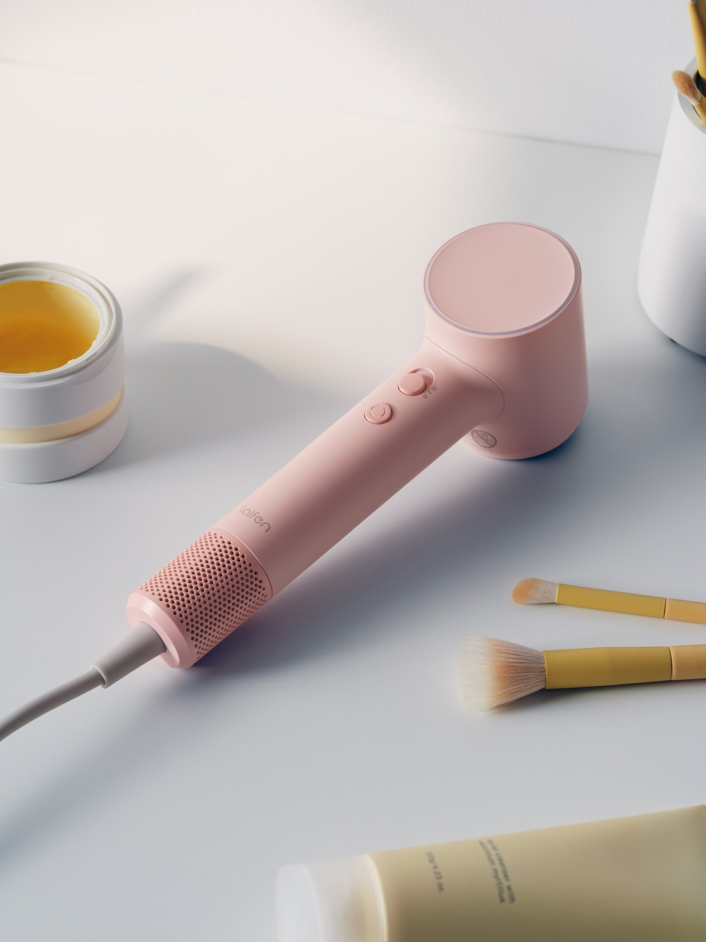 Różowa suszarka do włosów z kosmetykami na białym stole.