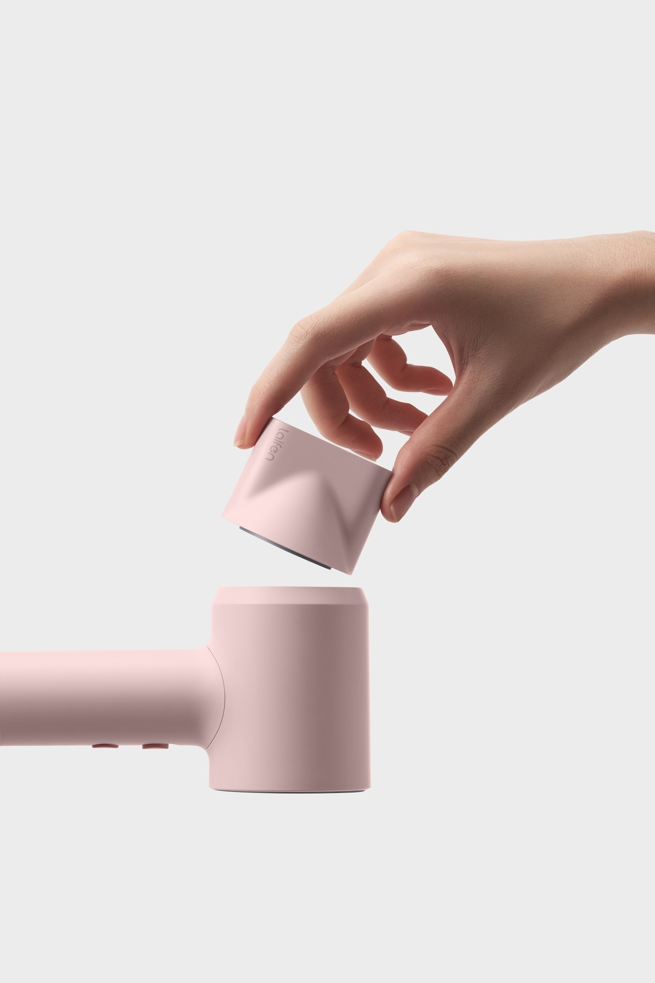 Dłoń trzyma różową nasadkę suszarki do włosów nad głównym urządzeniem.