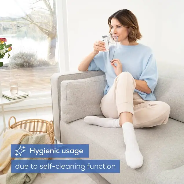 Femme assise sur un canapé avec un inhalateur. Fenêtre à l'arrière.