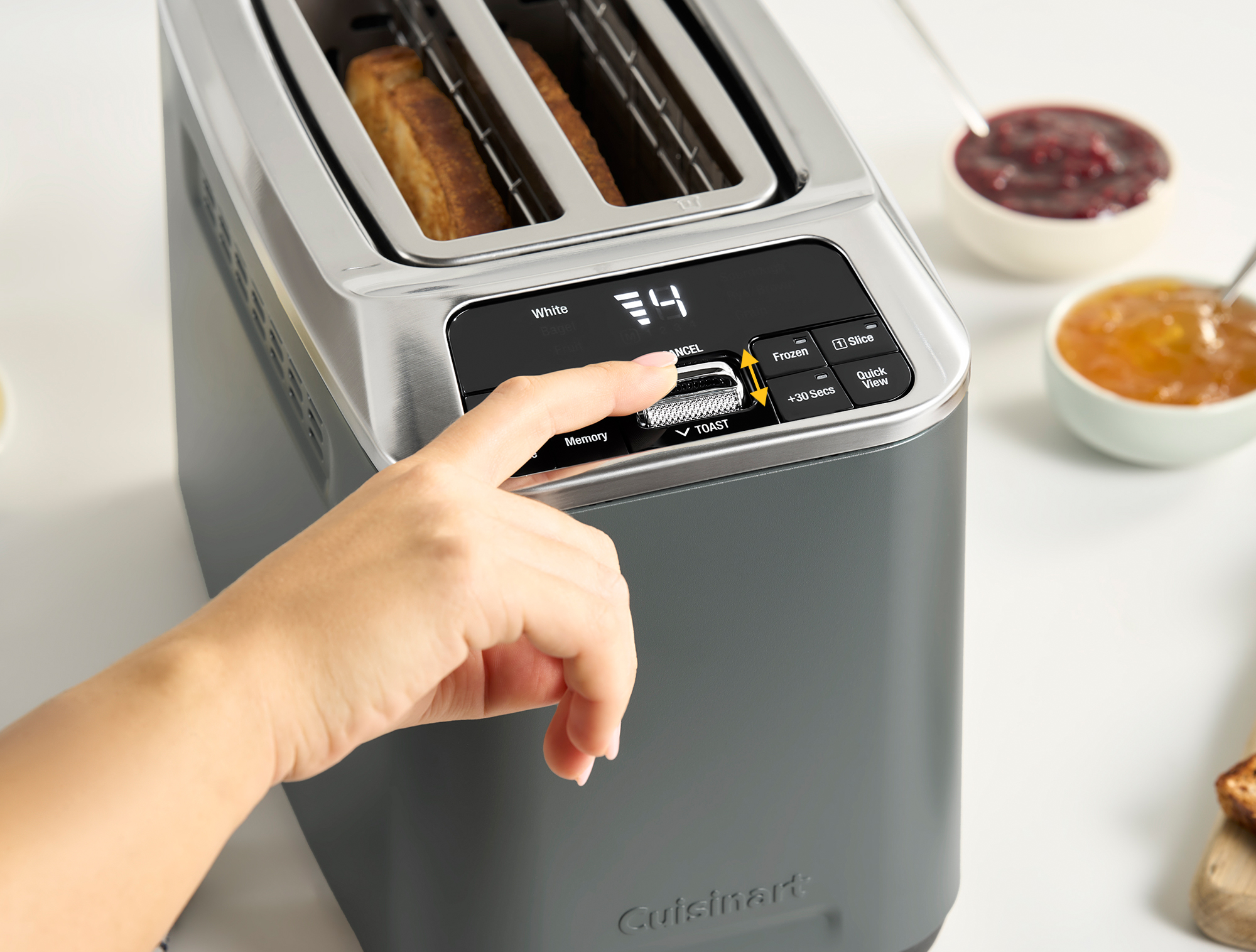 Une main actionne un grille-pain avec deux tranches de pain et deux bols de confiture.