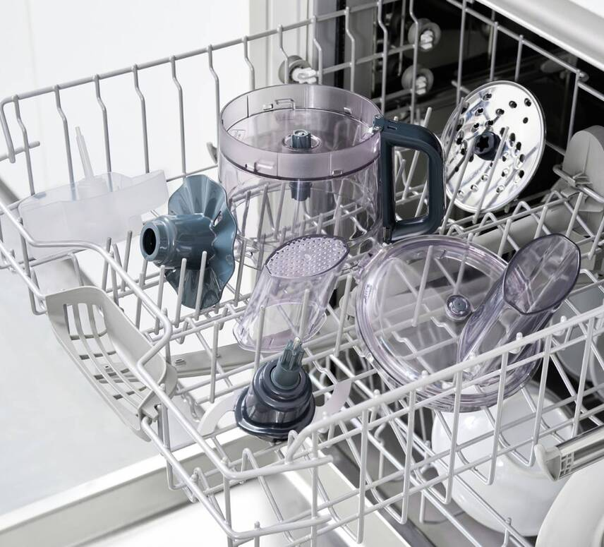 Parti di un robot da cucina in un cestello per lavastoviglie. Pezzi trasparenti e grigi.