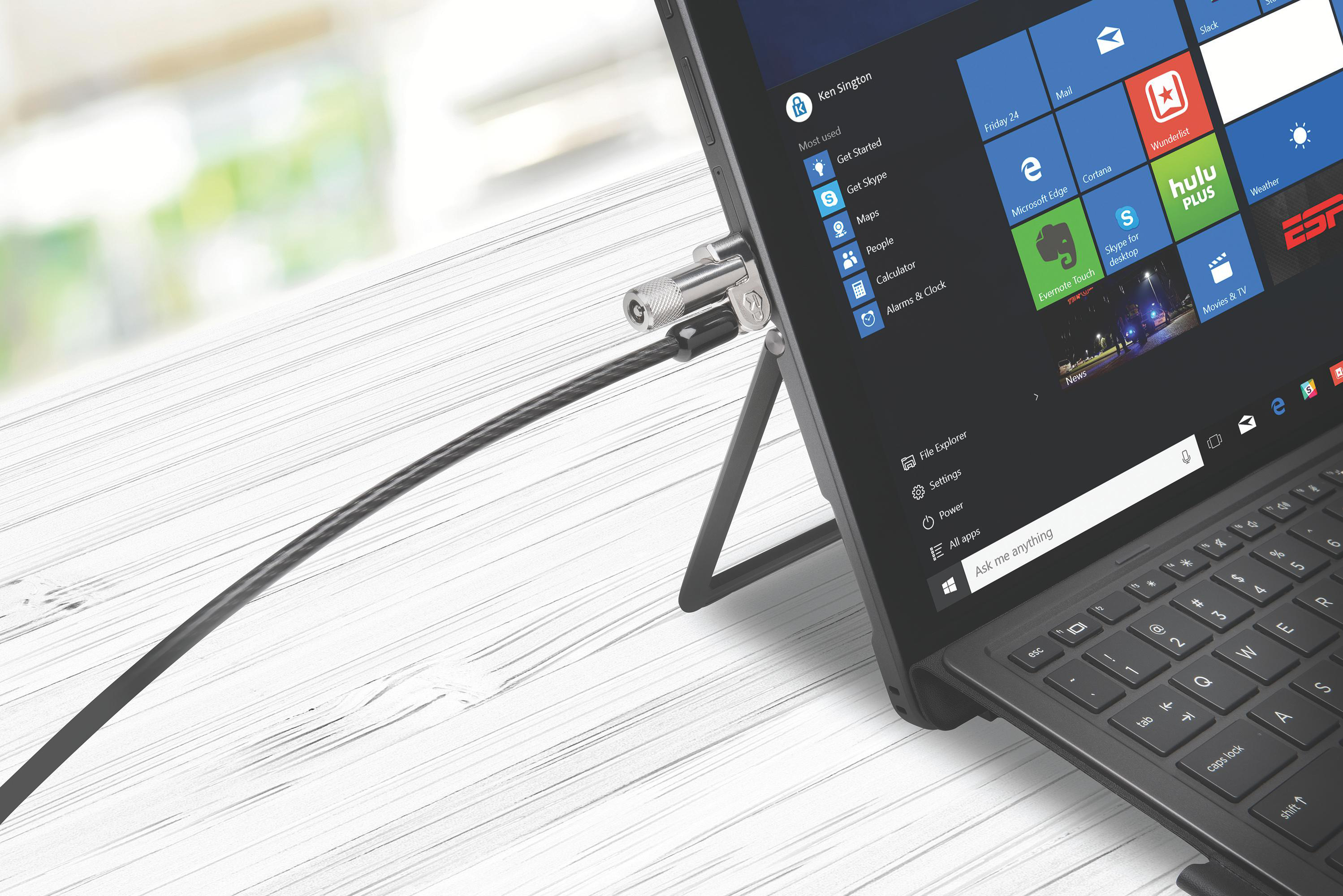 Ein Laptop mit einem Sicherheitsschloss und einem Kabel ist auf einem weißen Holztisch befestigt.