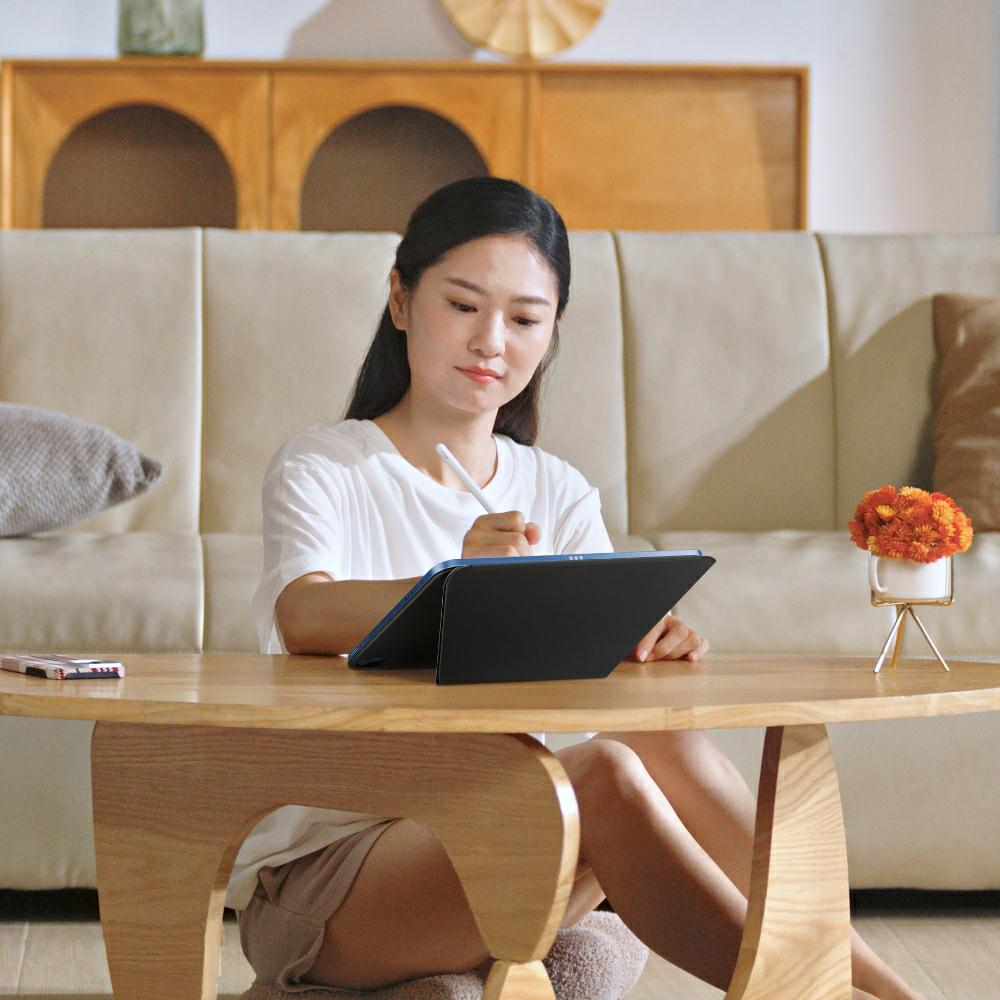 Kobieta siedzi na podłodze i pisze na tablecie rysikiem.