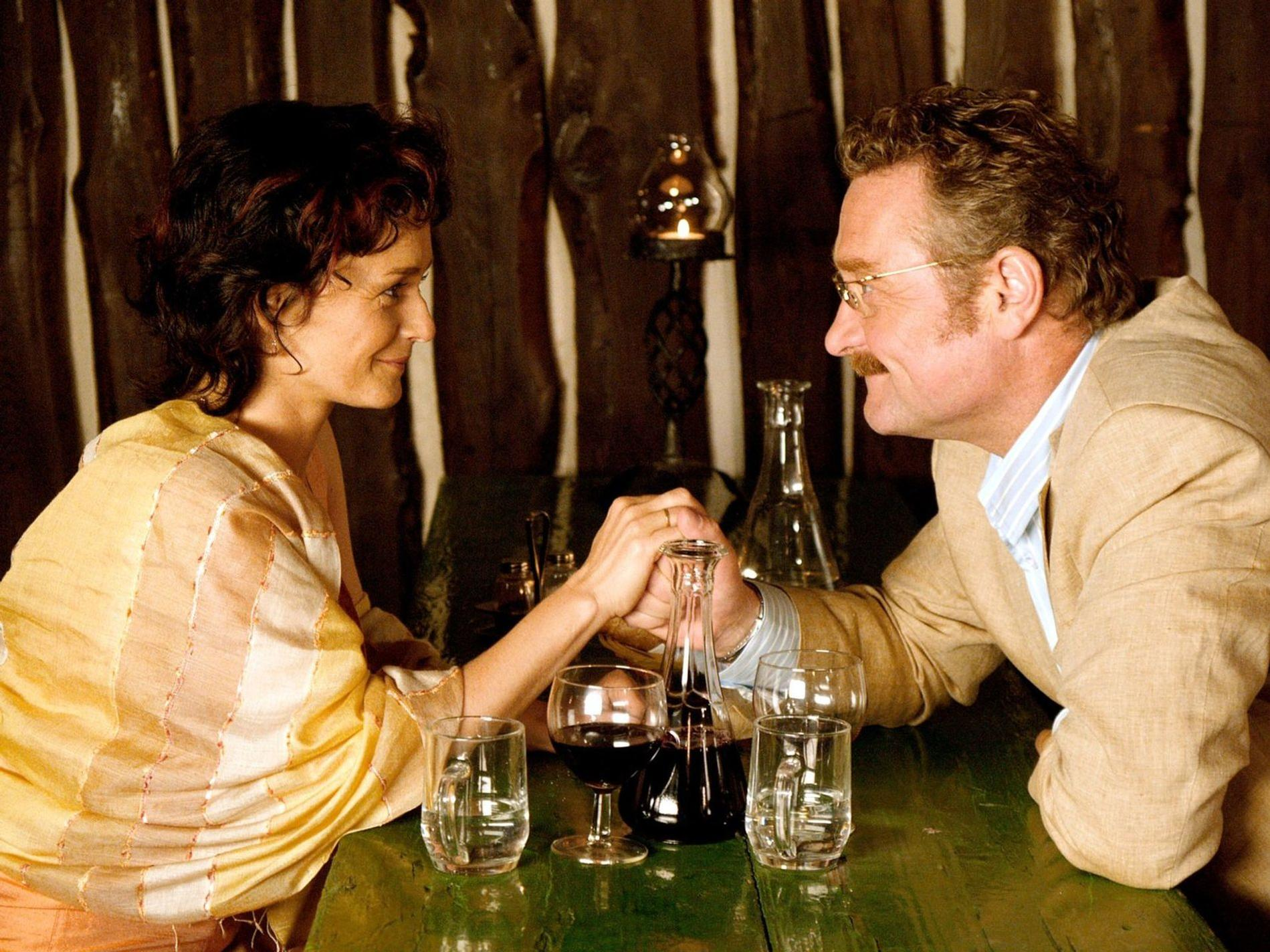 Ein Mann und eine Frau halten Händchen über einem Tisch mit Gläsern und Karaffen.