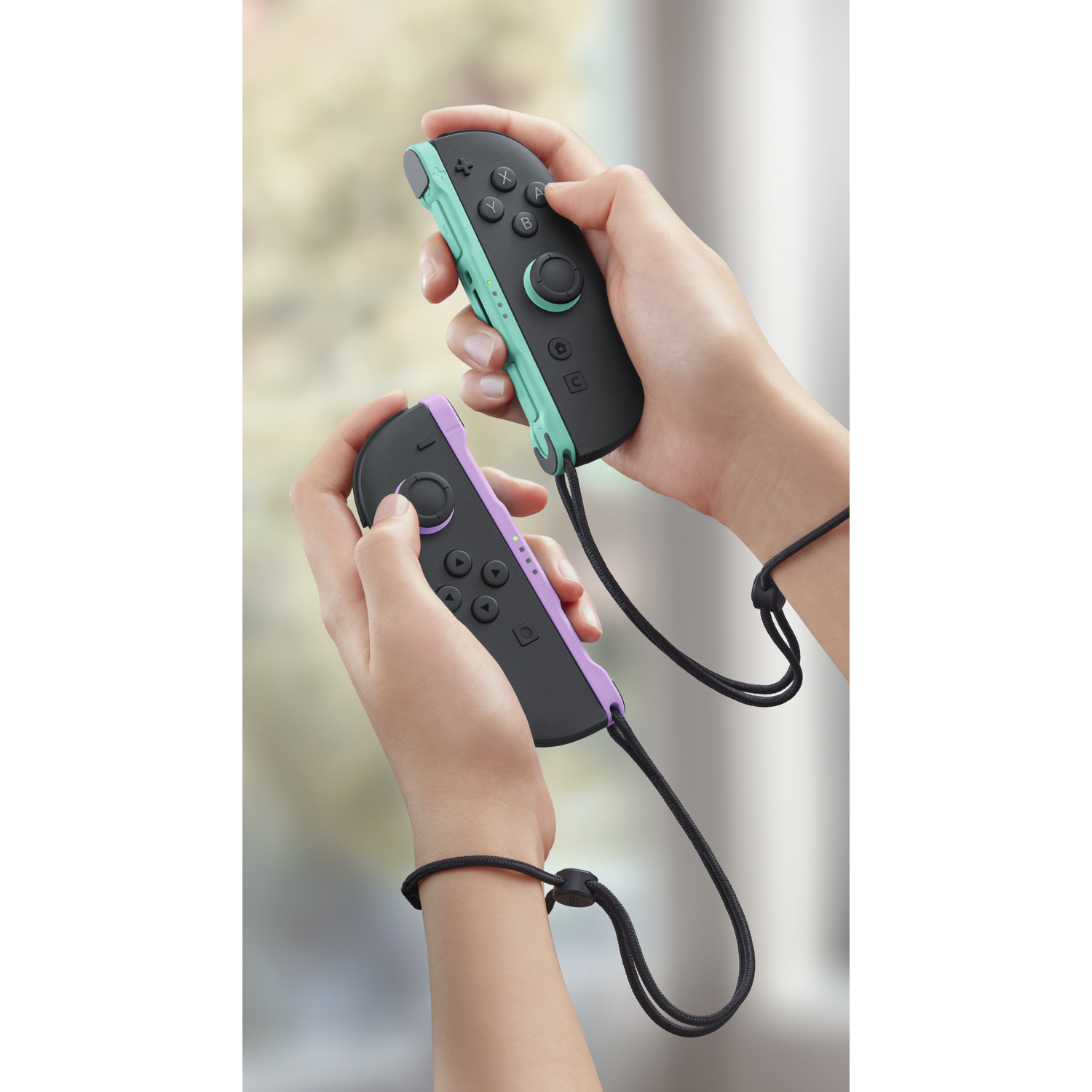 Hands holding two black controllers with mint green and purple accents.
