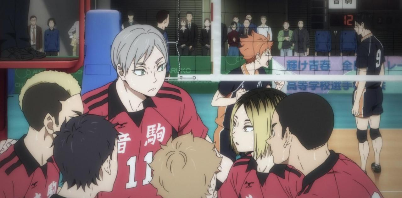 Ein Volleyballteam bespricht sich auf dem Spielfeld, einige Spieler tragen rote Trikots.