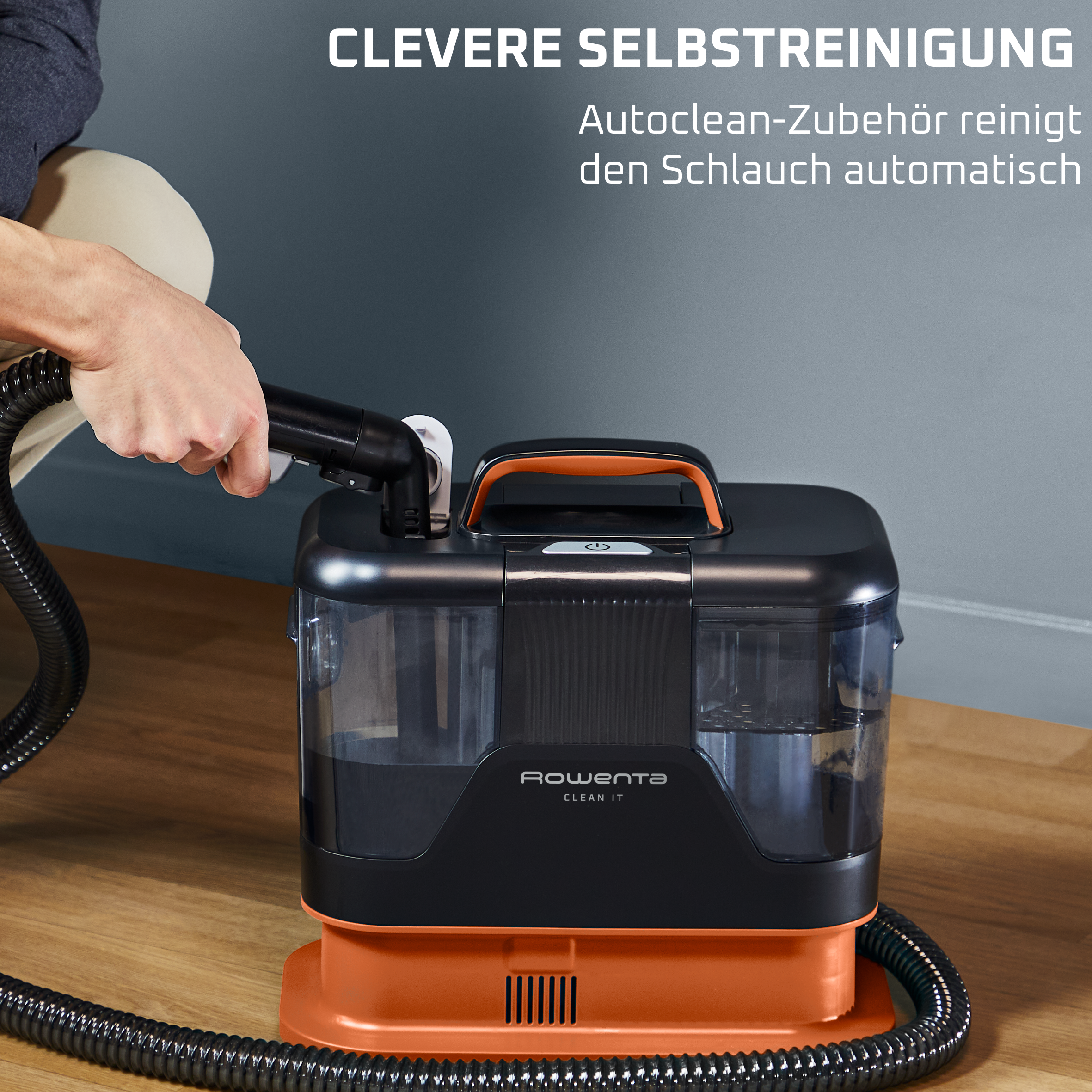 Ein Mann hält einen Schlauchanschluss an einem schwarzen und orangen Reinigungsgerät.