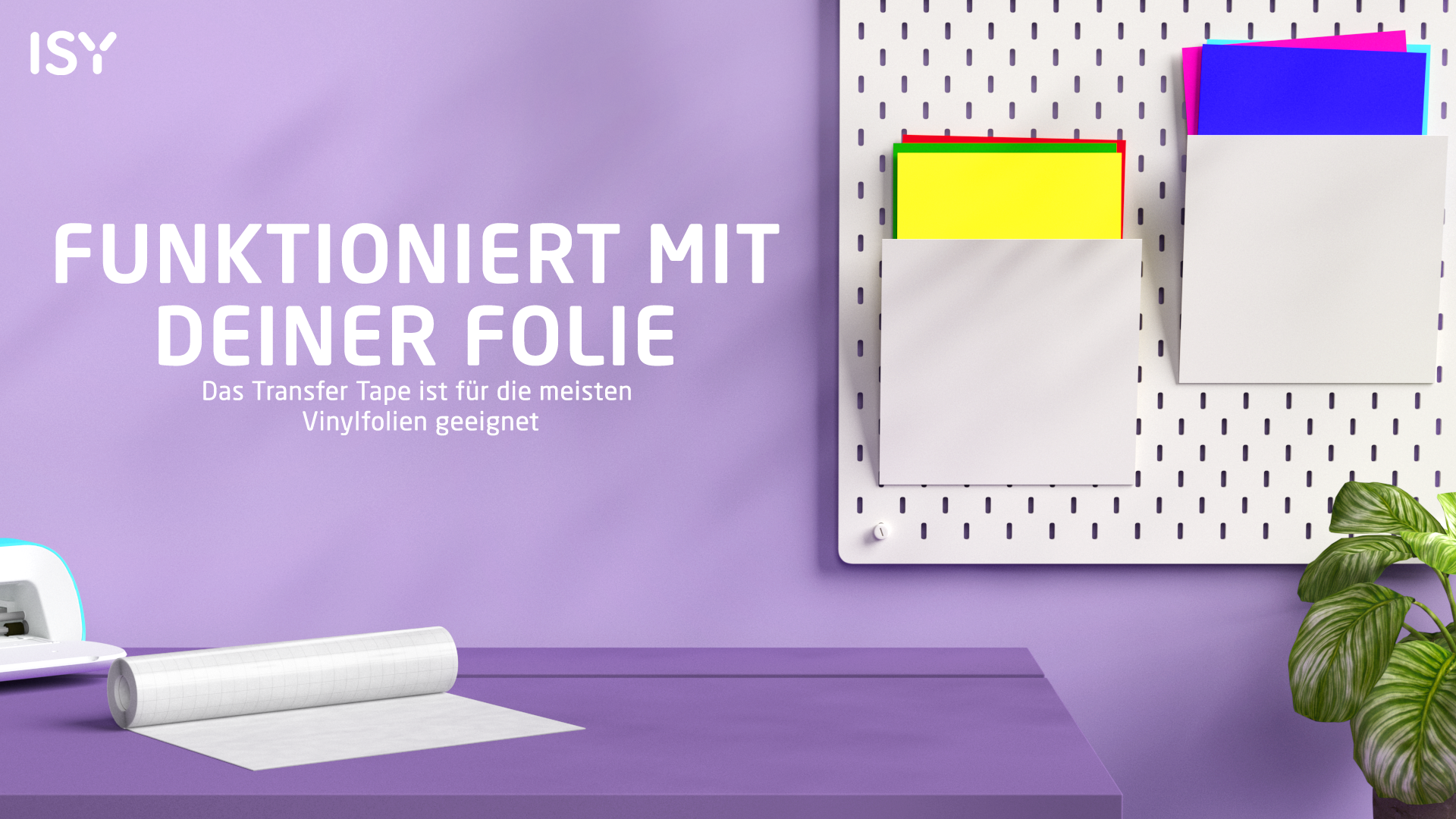 Ein Schreibtisch mit Transferfolie, einem Schneidegerät und bunten Papieren an einer Wand.