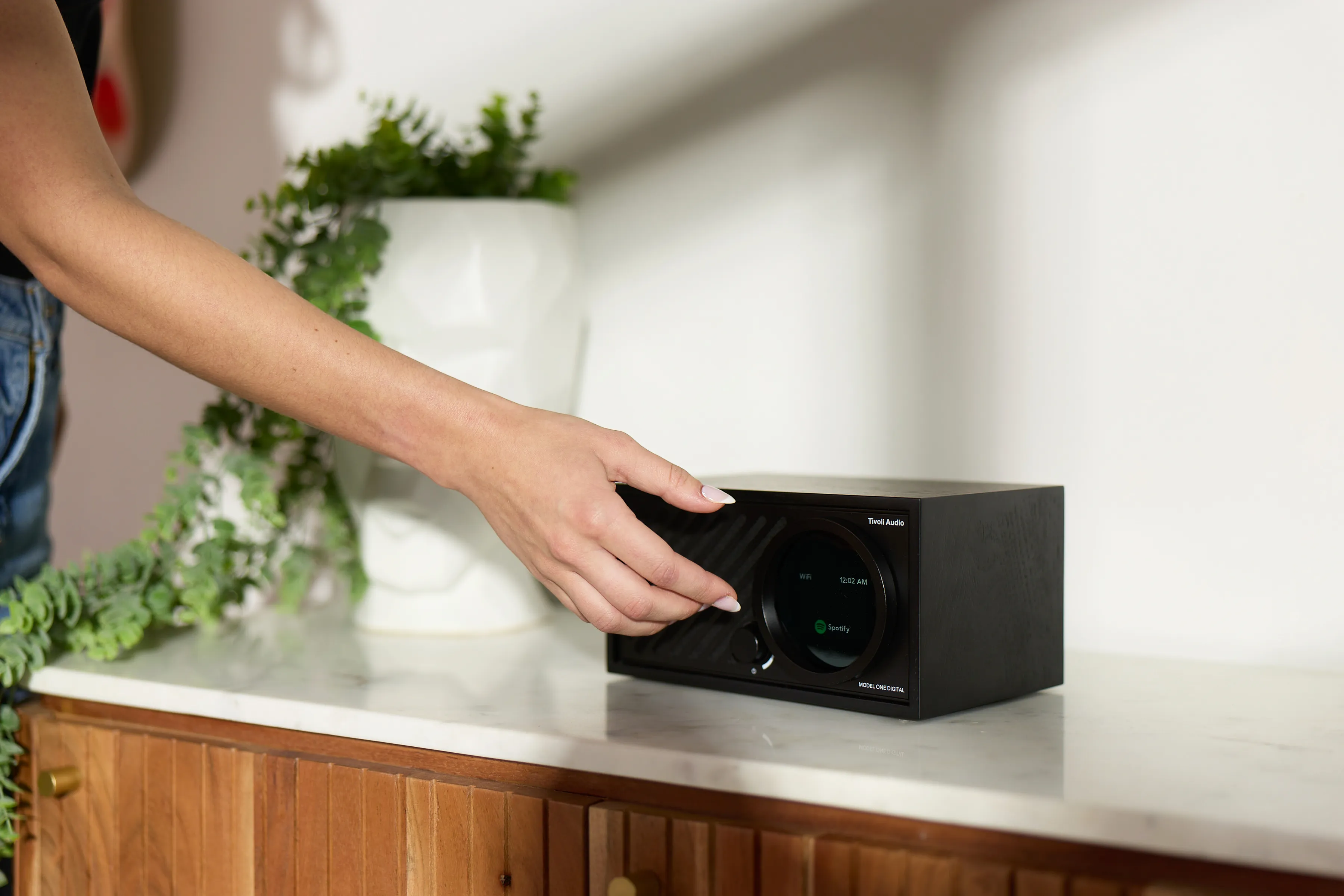 Eine Hand berührt einen schwarzen Tivoli Audio Lautsprecher auf einem Marmortisch.