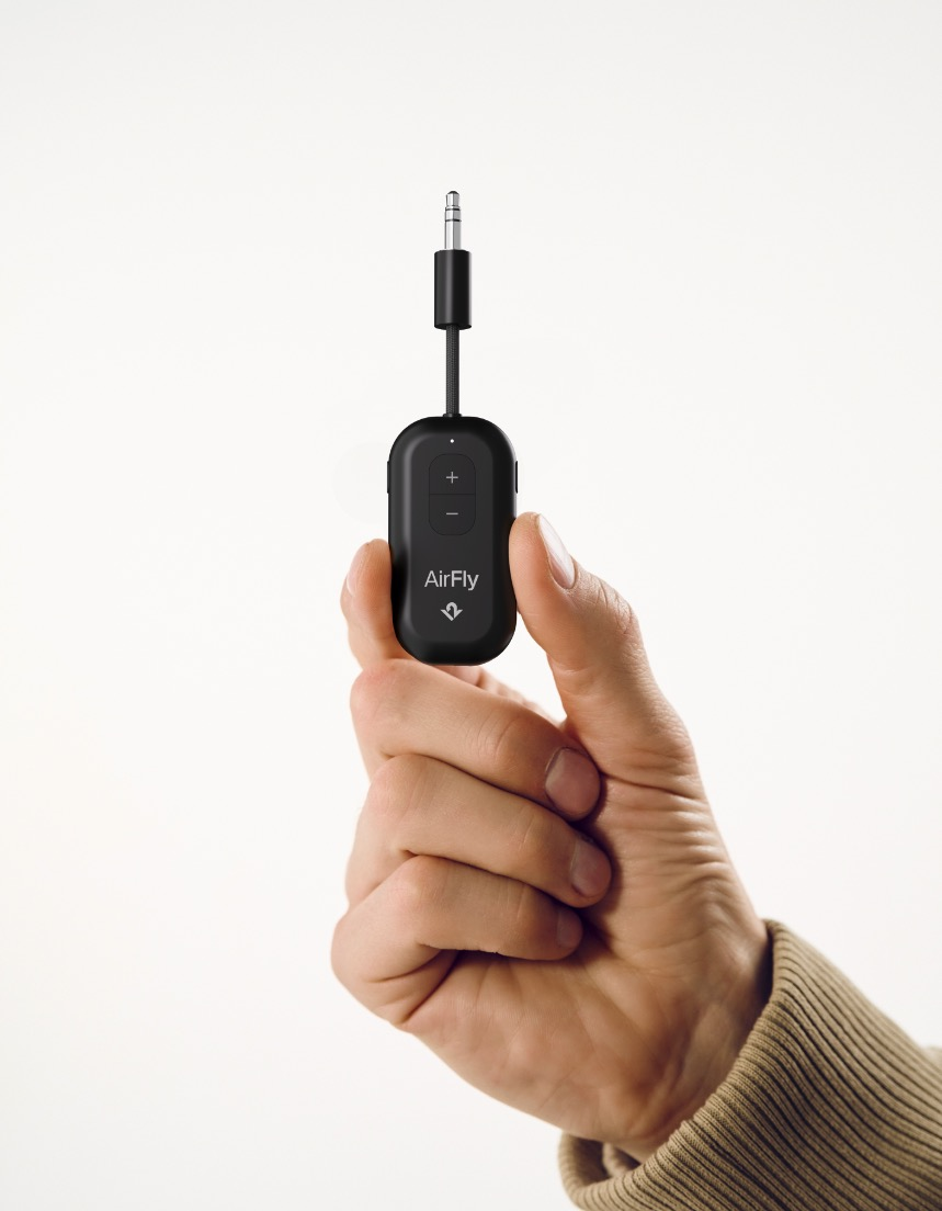Une main tient un petit appareil AirFly noir avec une prise jack de 3,5 mm.