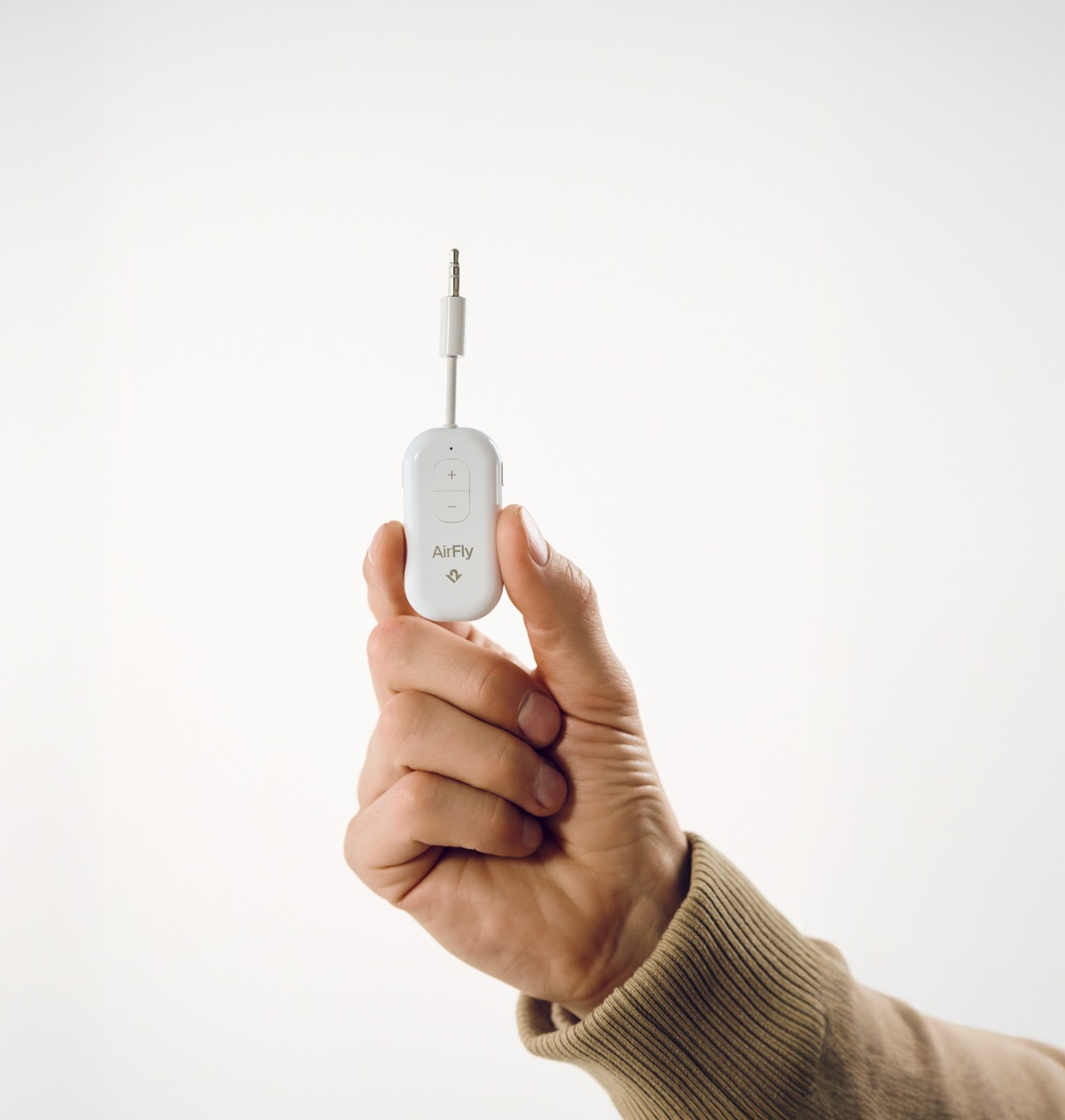 Une main tient un petit appareil blanc AirFly avec une prise jack.