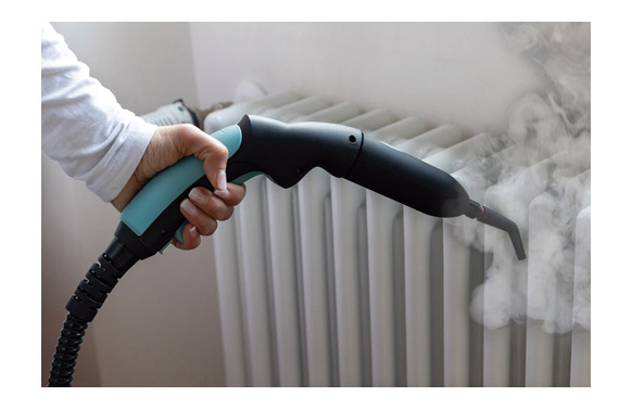 Una mano sostiene un limpiador a vapor que rocía vapor sobre un radiador.