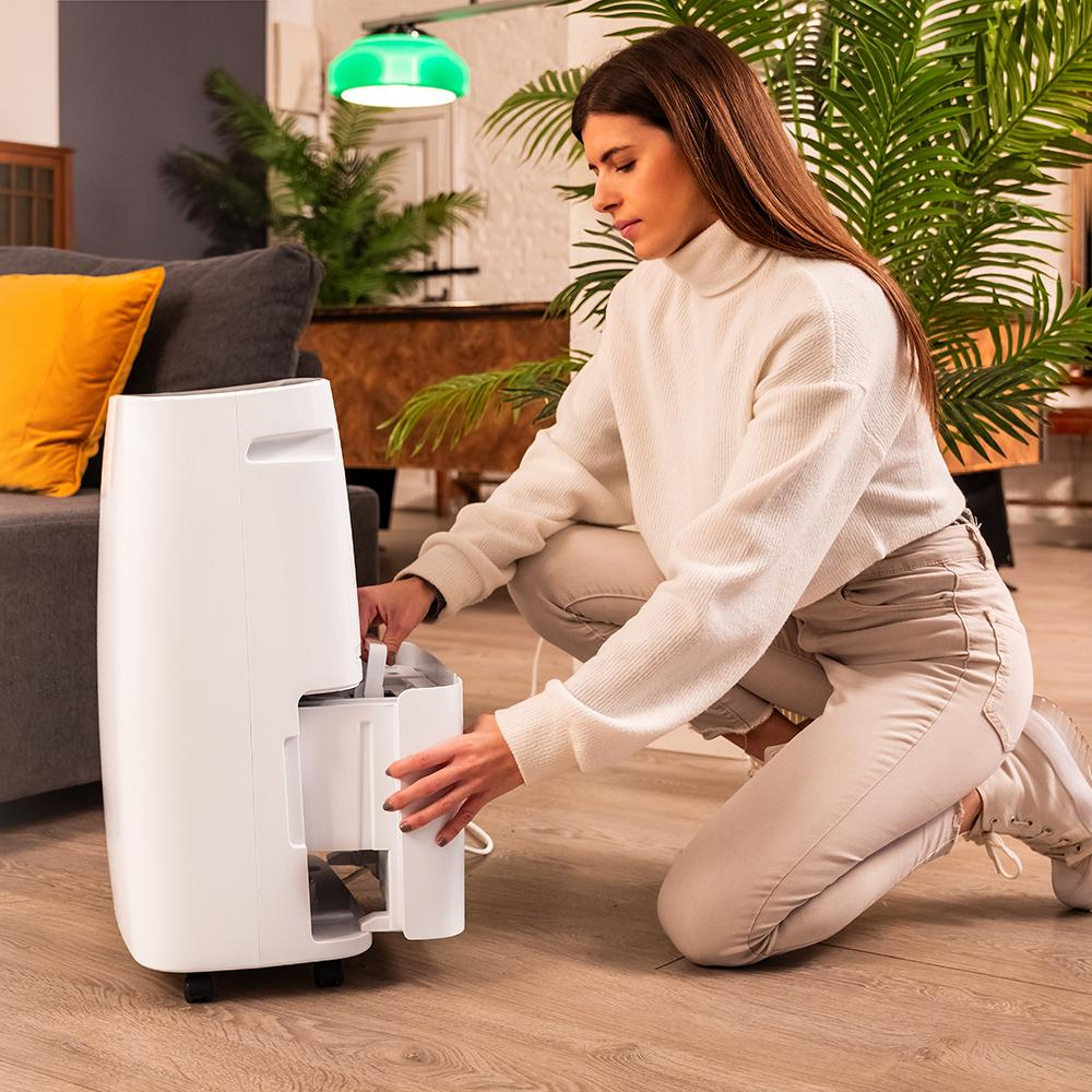 Mujer arrodillada junto a deshumidificador blanco, sacando un cajón.