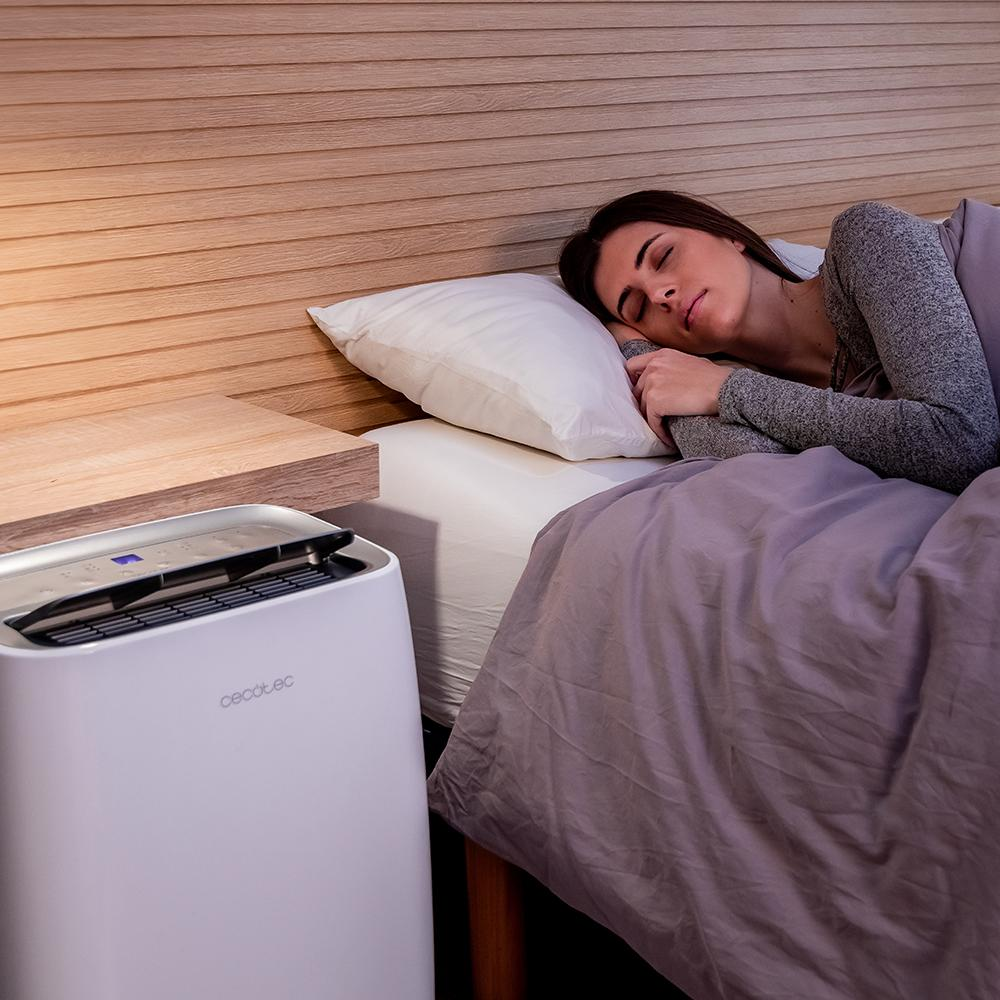 Mujer durmiendo en la cama junto a un purificador de aire blanco.