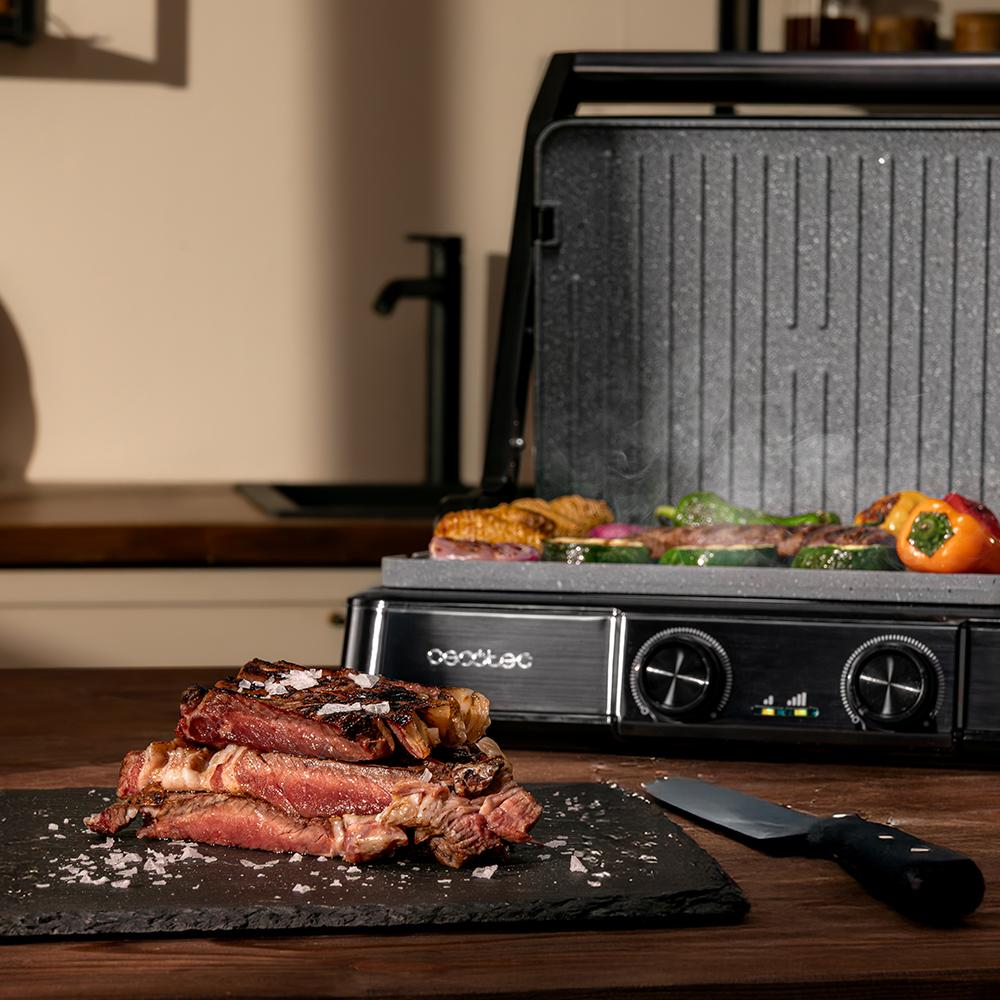 Una pila de bistec sobre piedra junto a una parrilla con verduras.