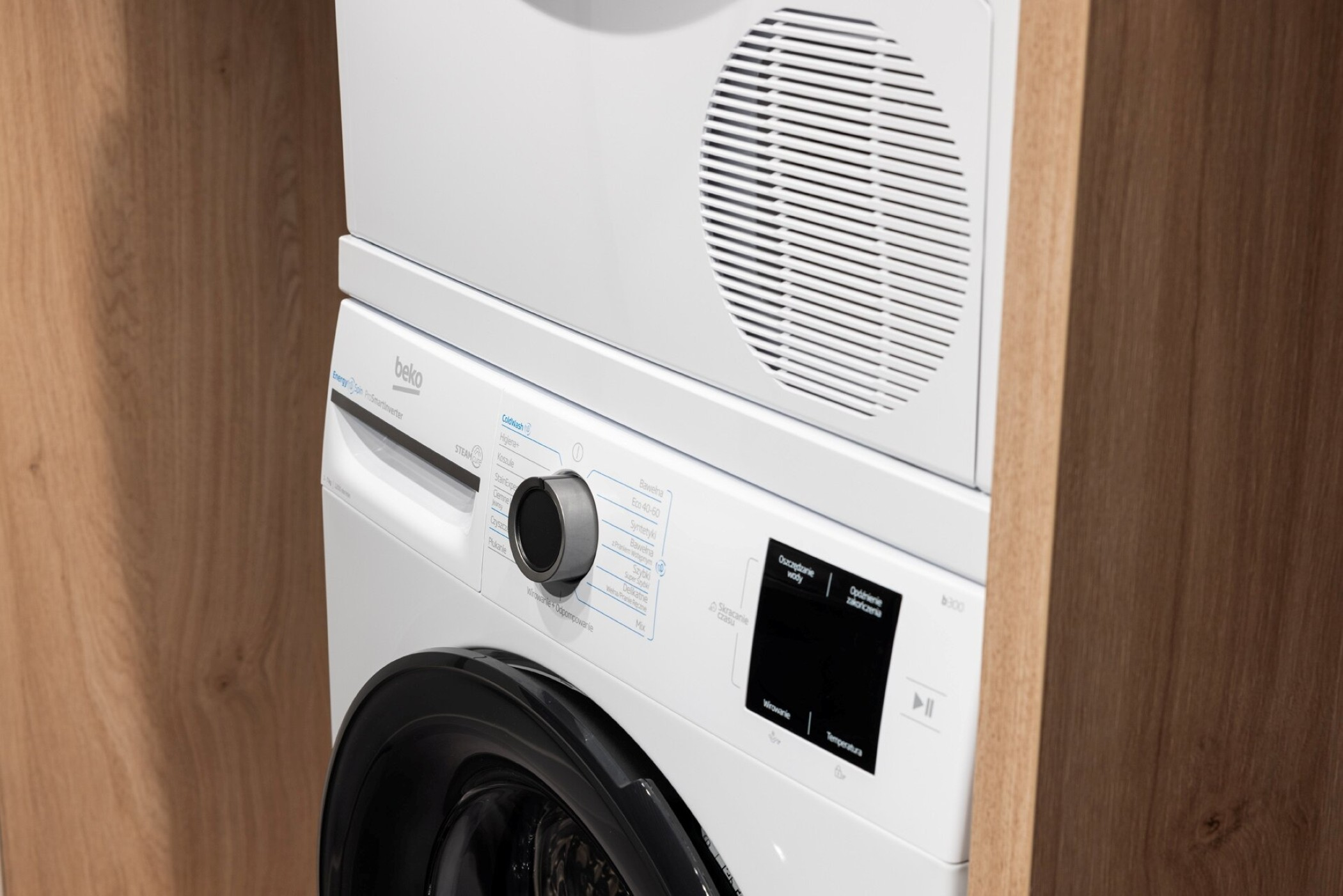 Biała pralka Beko z panelem sterowania obok drewnianego laminatu.