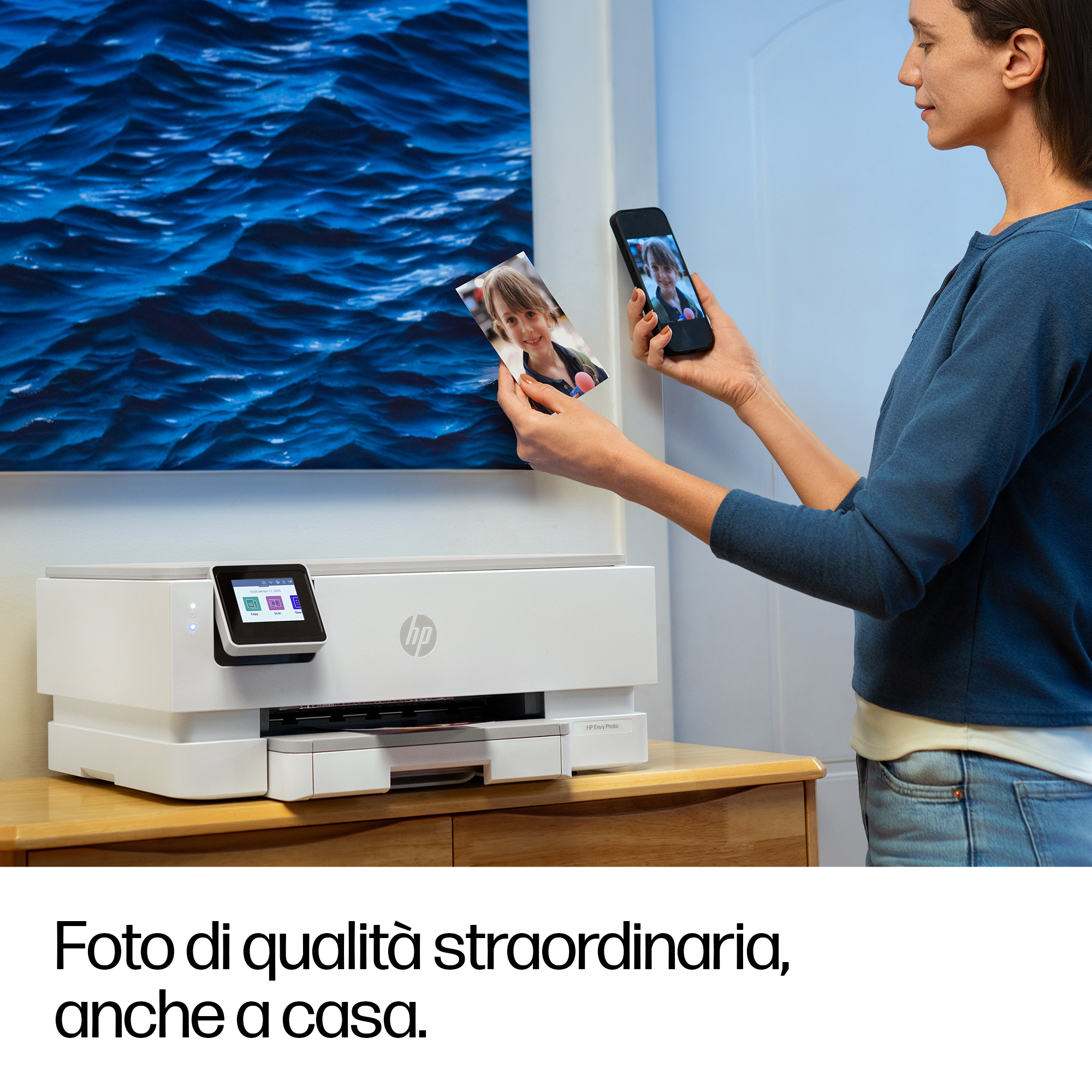 Una donna tiene una foto e uno smartphone davanti a una stampante e un quadro di onde.