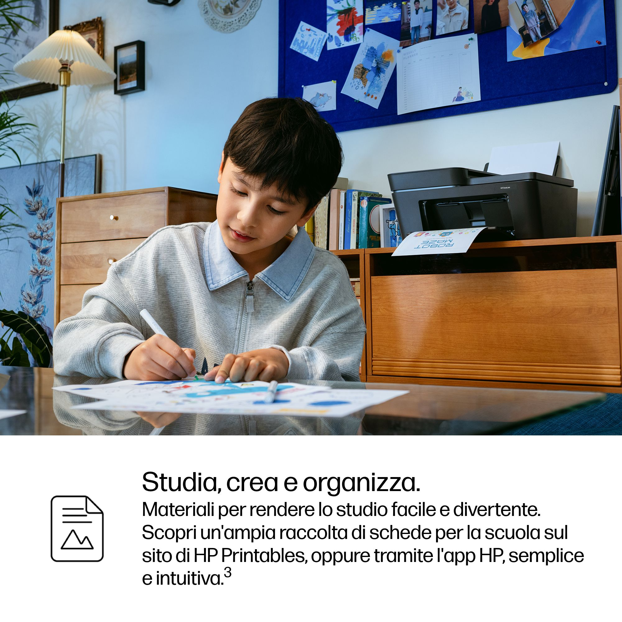 Un ragazzo disegna a una scrivania con una stampante sullo sfondo.