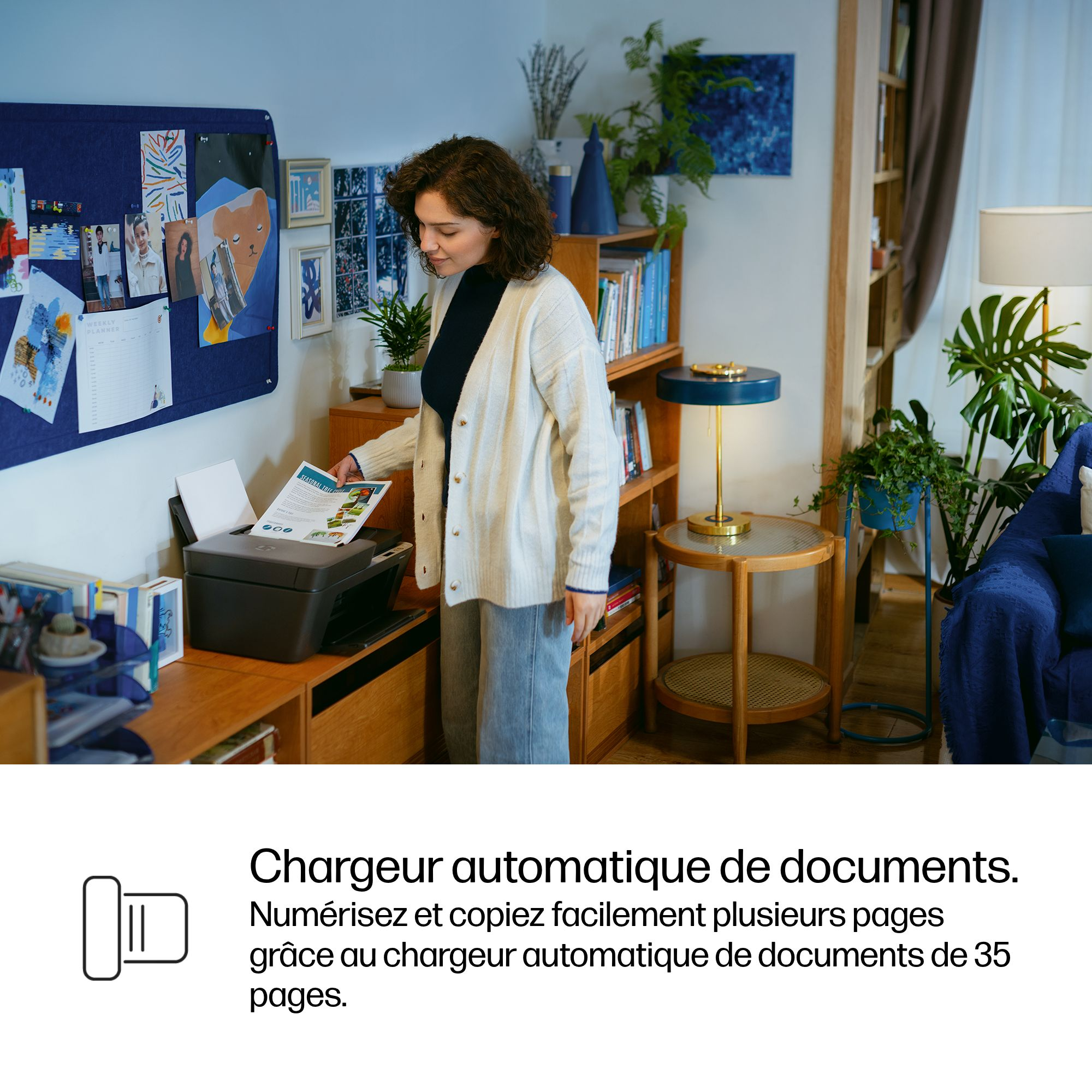 Une femme aux cheveux bouclés met un document dans une imprimante. Un bureau avec des plantes.