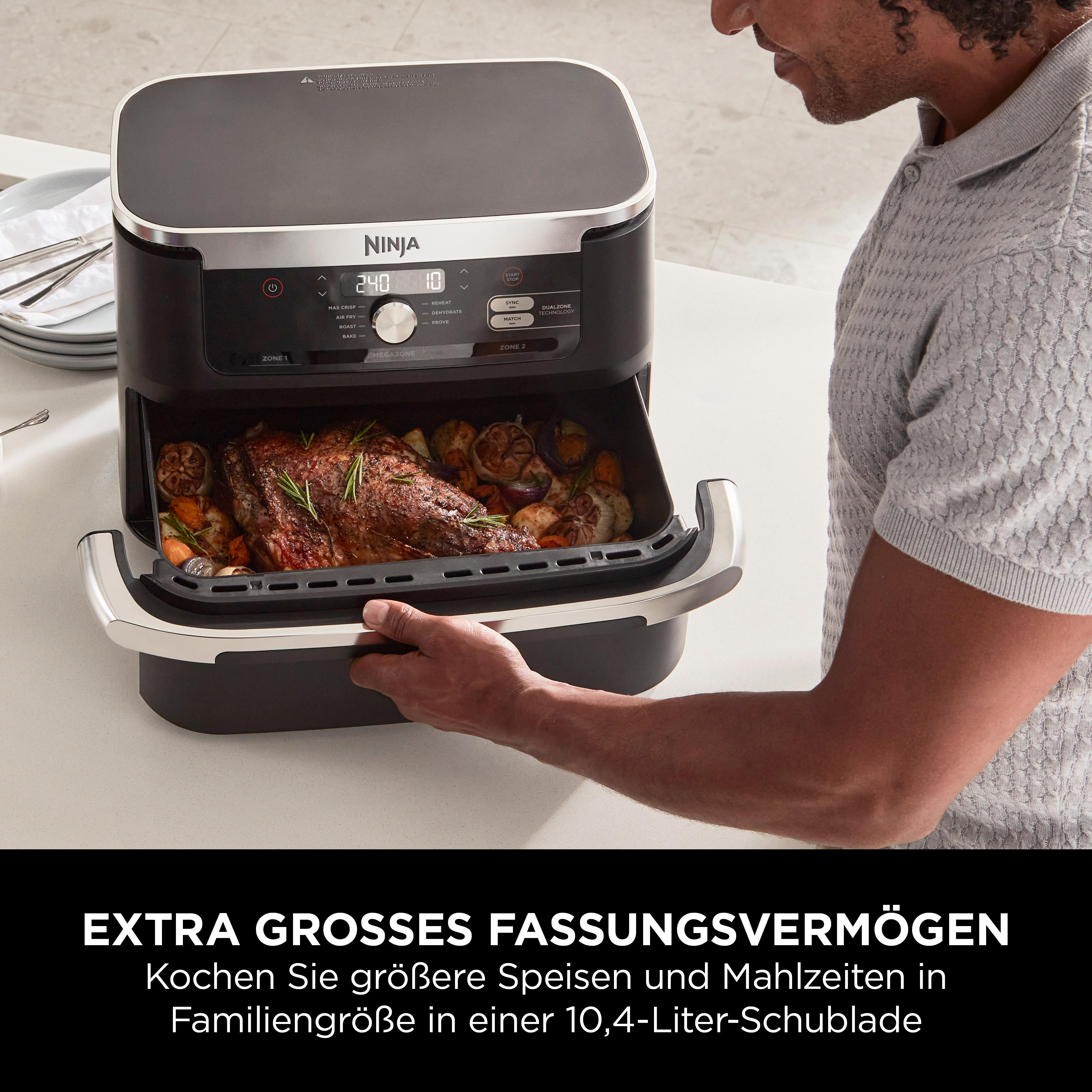 Ein Mann zieht eine Schublade eines schwarzen Airfryers heraus, gefüllt mit Braten und Gemüse.