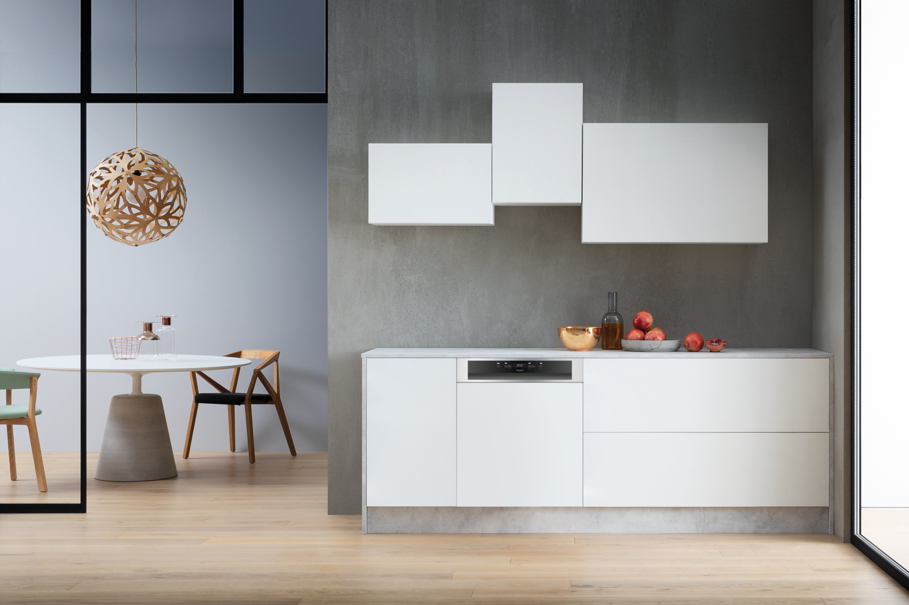 Nowoczesna kuchnia z białymi szafkami, miską na owoce, butelką i jabłkami.