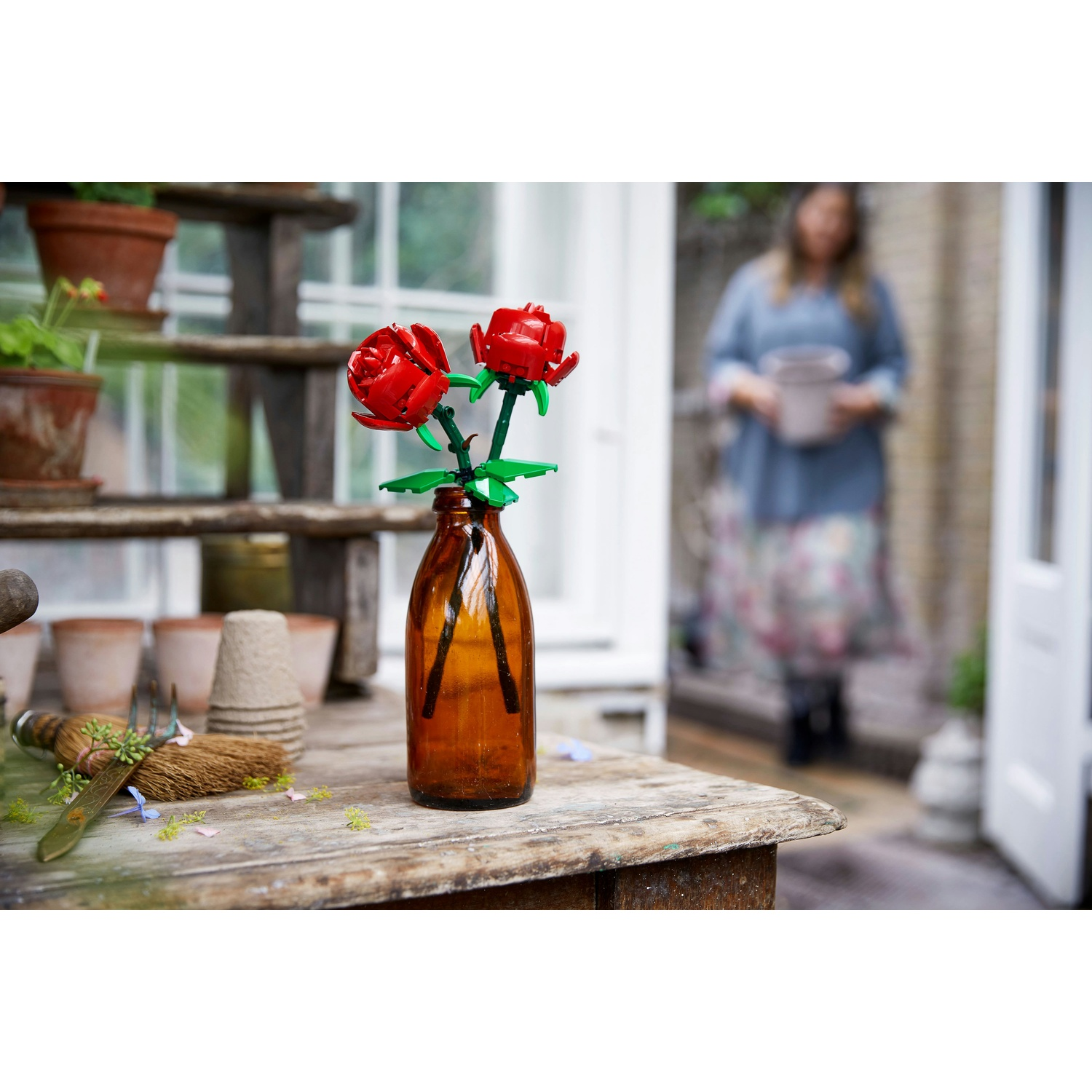 Due rose rosse Lego in una bottiglia di vetro marrone su un tavolo di legno.