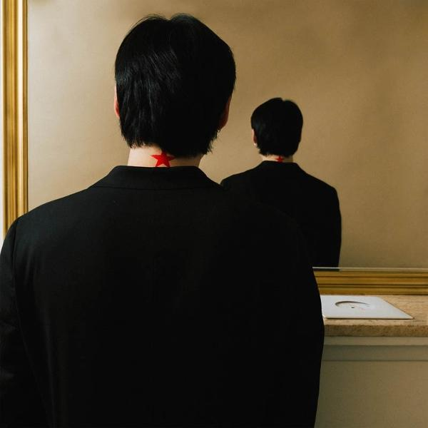 Person im schwarzen Anzug blickt in Spiegel, roter Stern am Nacken.